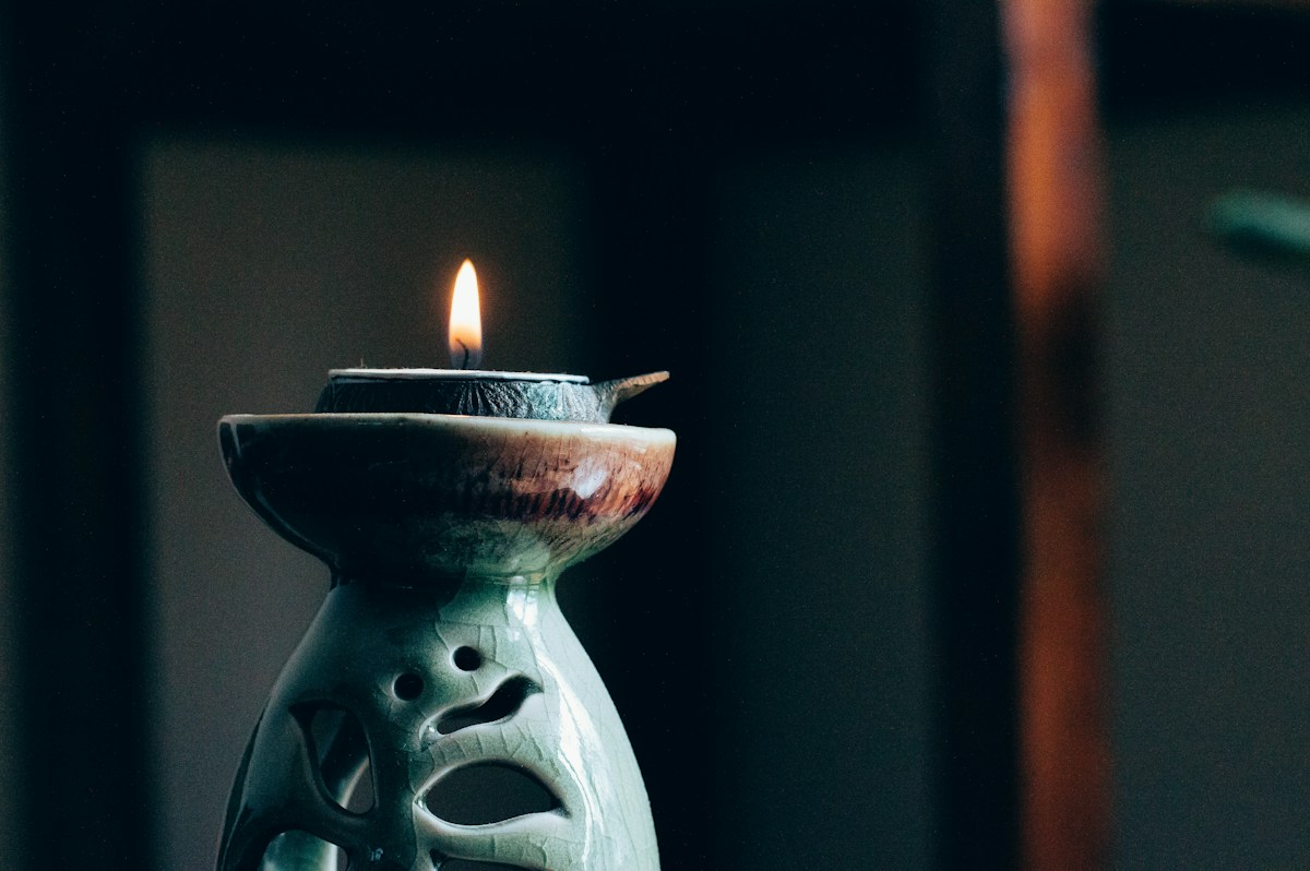 A lit candle on a ceramic oil burner in a dark, quiet room