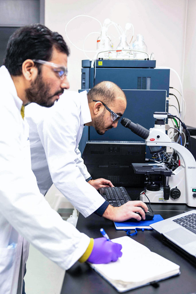 SteriMax scientists examining a sample under a microscope while a colleague records notes in a laboratory.