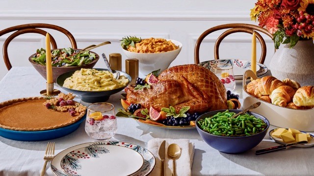 Imagen de mesa de Thanksgiving con un pavo y diferentes platillos para compartir en familia