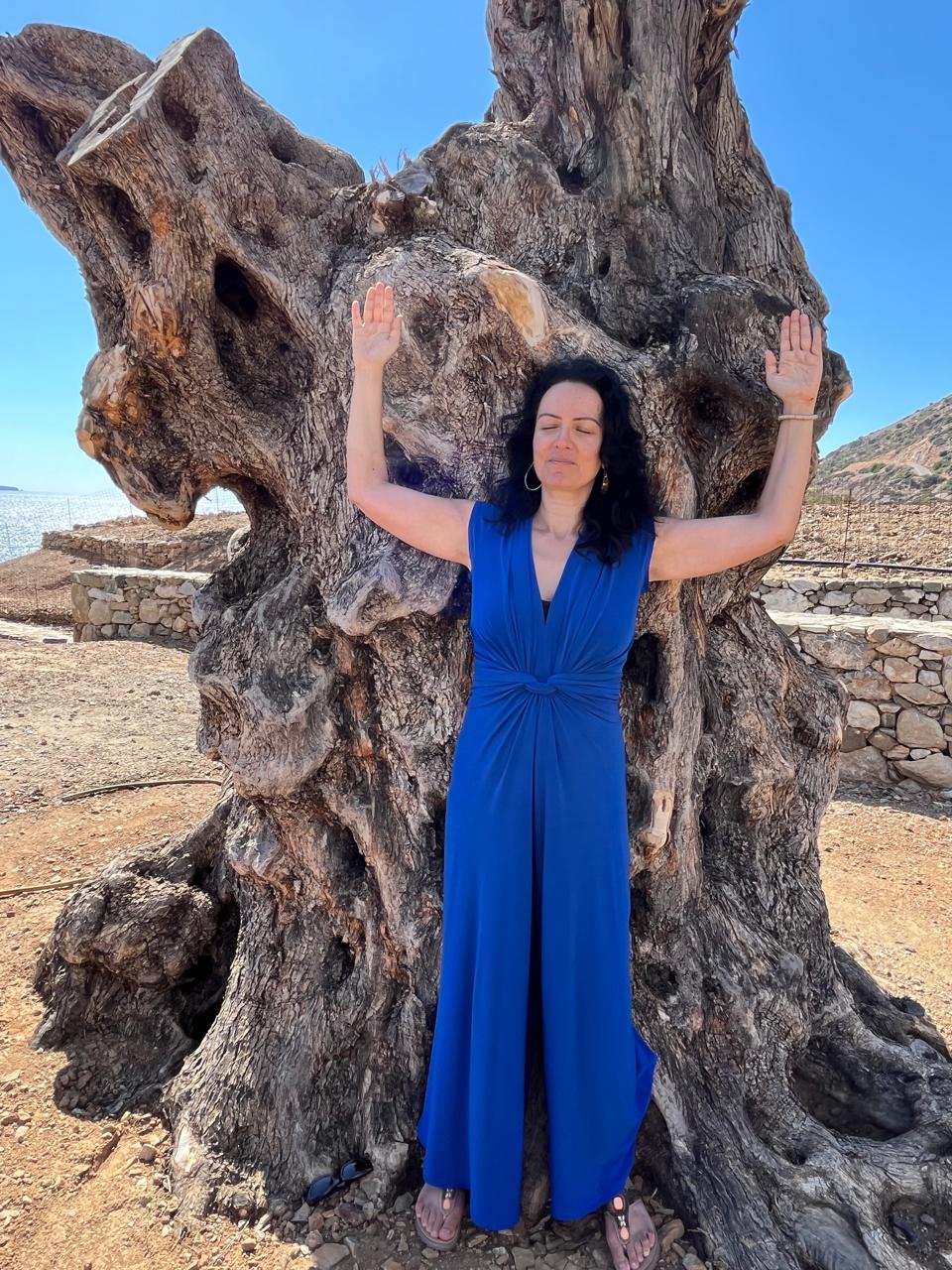 A young woman with long dark hair smiles confidently while crossing her arms in a modern indoor setting.