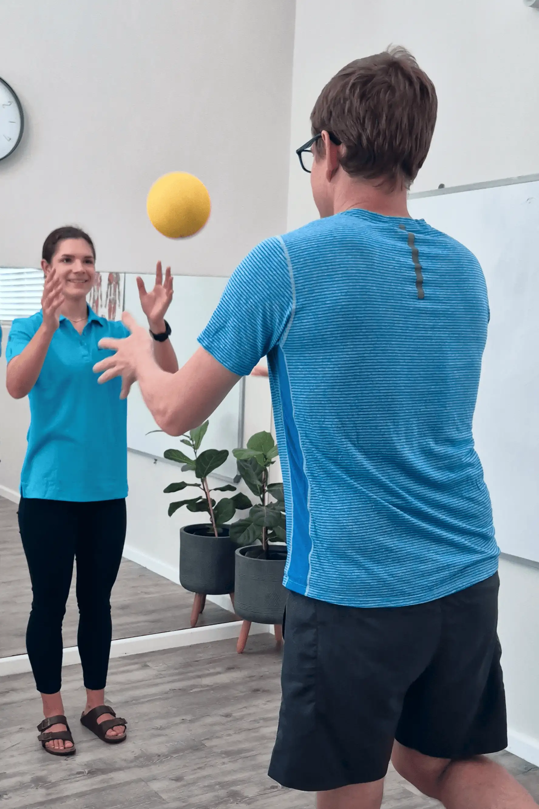 A patient balancing on one leg throws a yellow ball to a physiotherapist for concussion balance retraining.