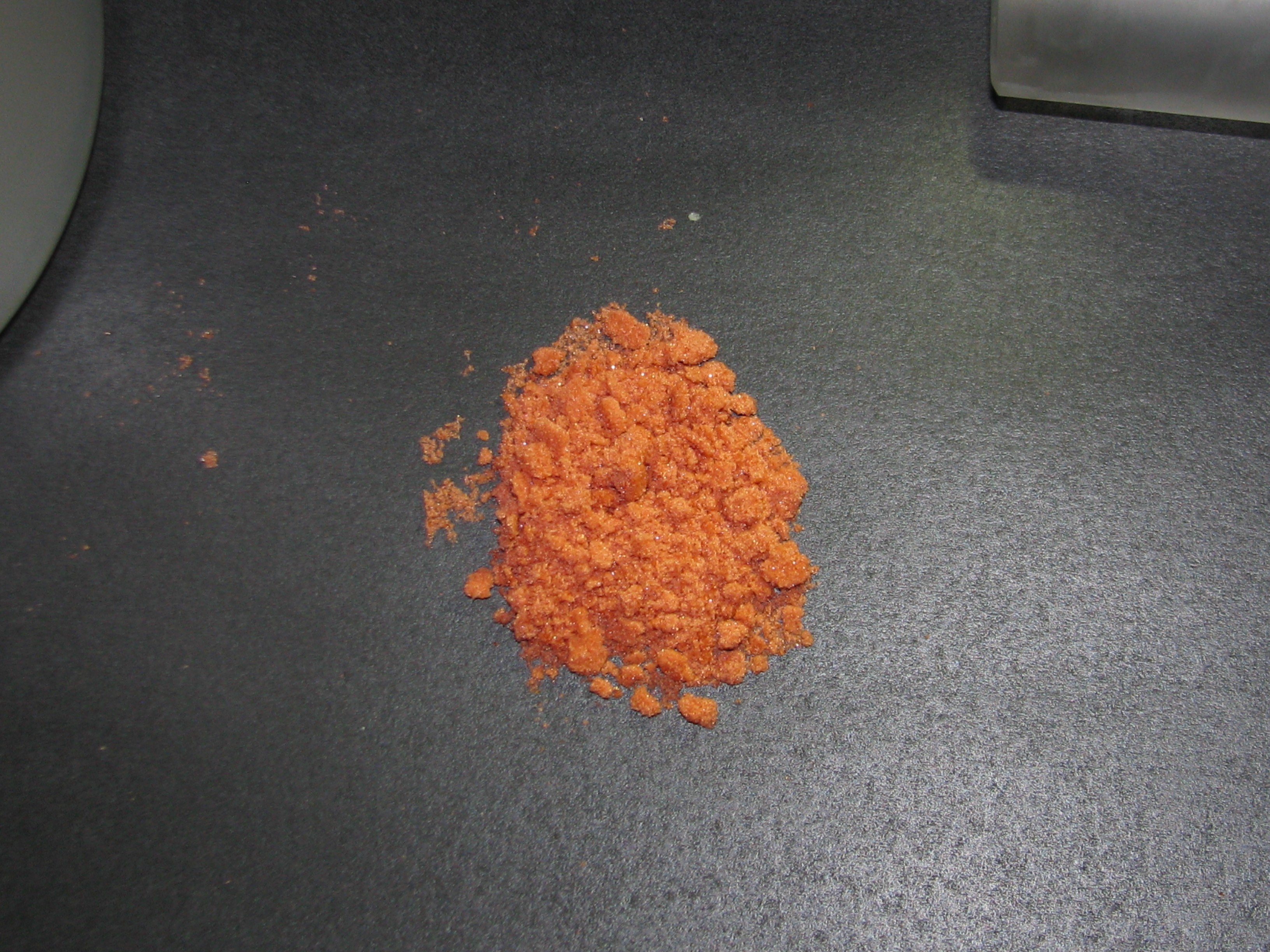 Orange cobalt sulphate crystals on a dark laboratory work surface.
