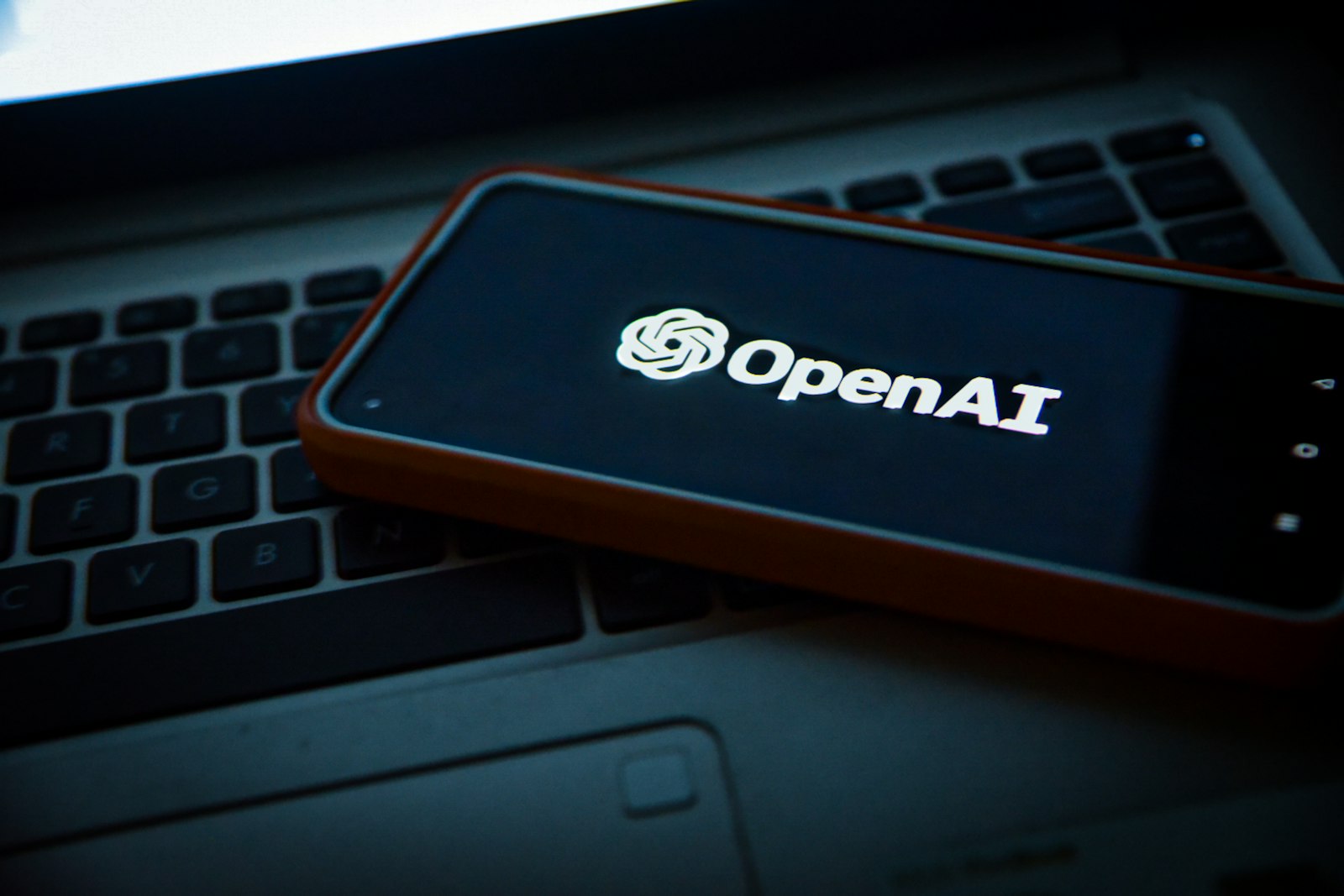 Smartphone met het OpenAI-logo op een laptoptoetsenbord, symbool voor adverteren in ChatGPT via de nieuwe self-serve Ads Manager