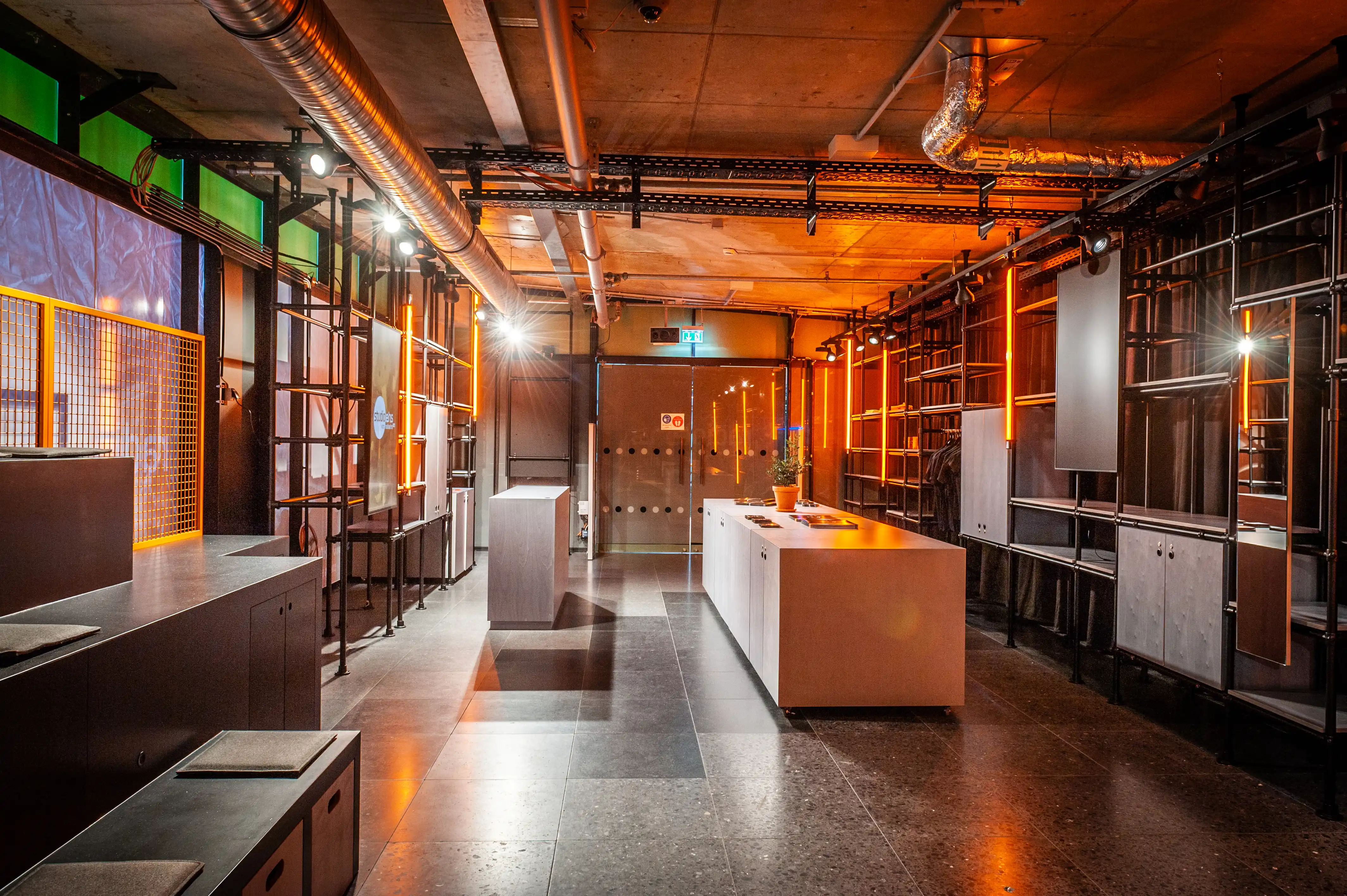 View through the Radio Eins studio with copper-toned ceiling, exposed ducts, wooden islands and orange light accents.