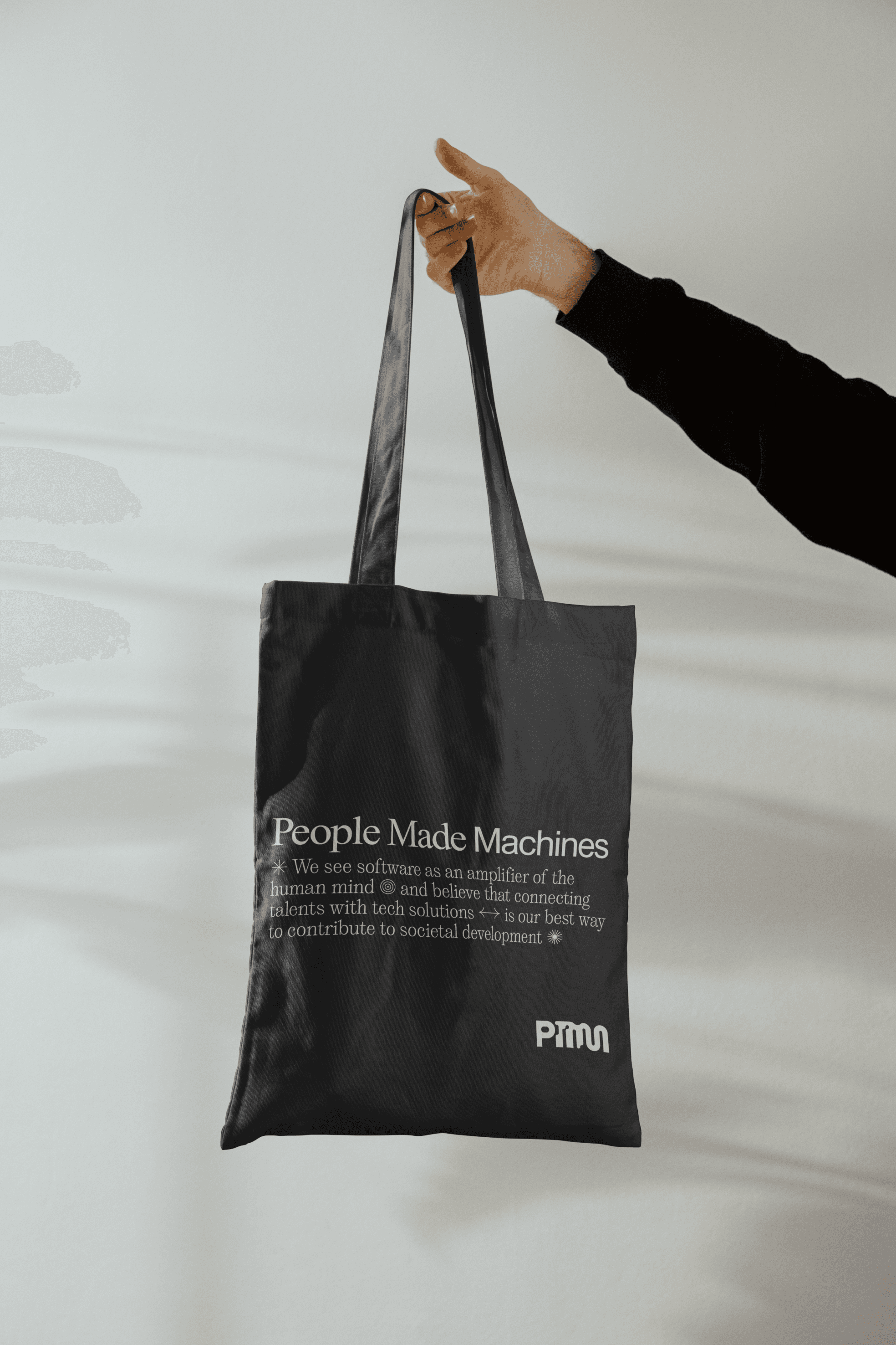 Image of a person holding a black cotton totebag with People Made Machines messaging and logo.