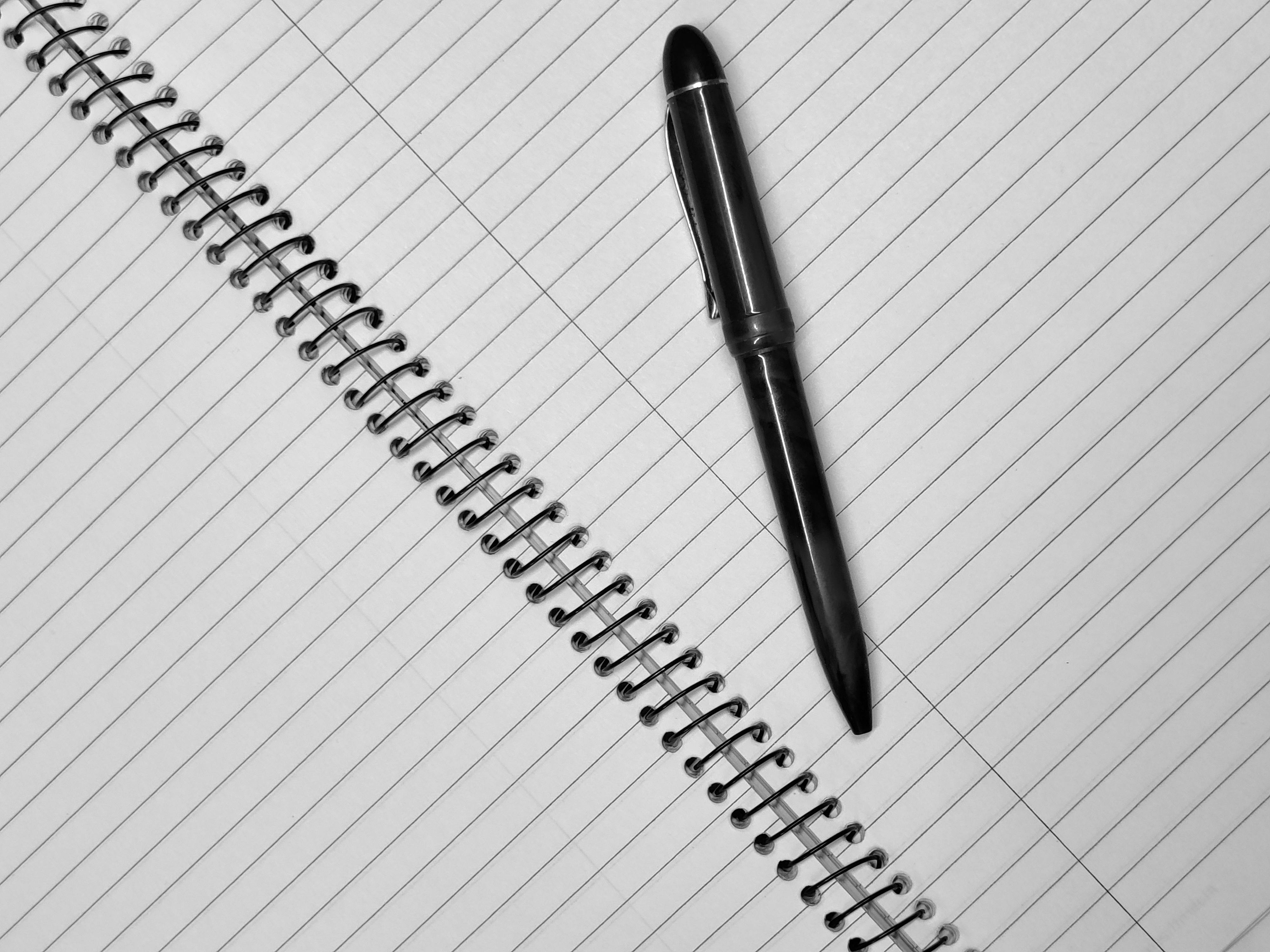 black-and-white-image-of-a-spiral-bound-notebook-with-a-pen-placed-diagonally.-i - rahul-shah (pexels)