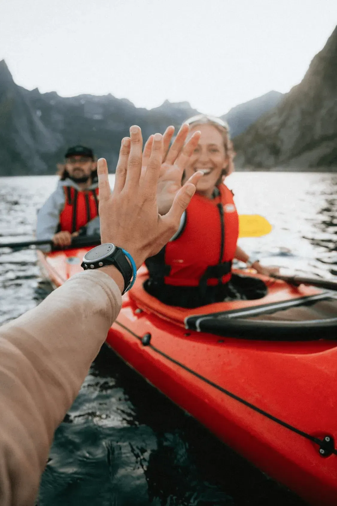 Kayakers giving a high five on a mountain lake.