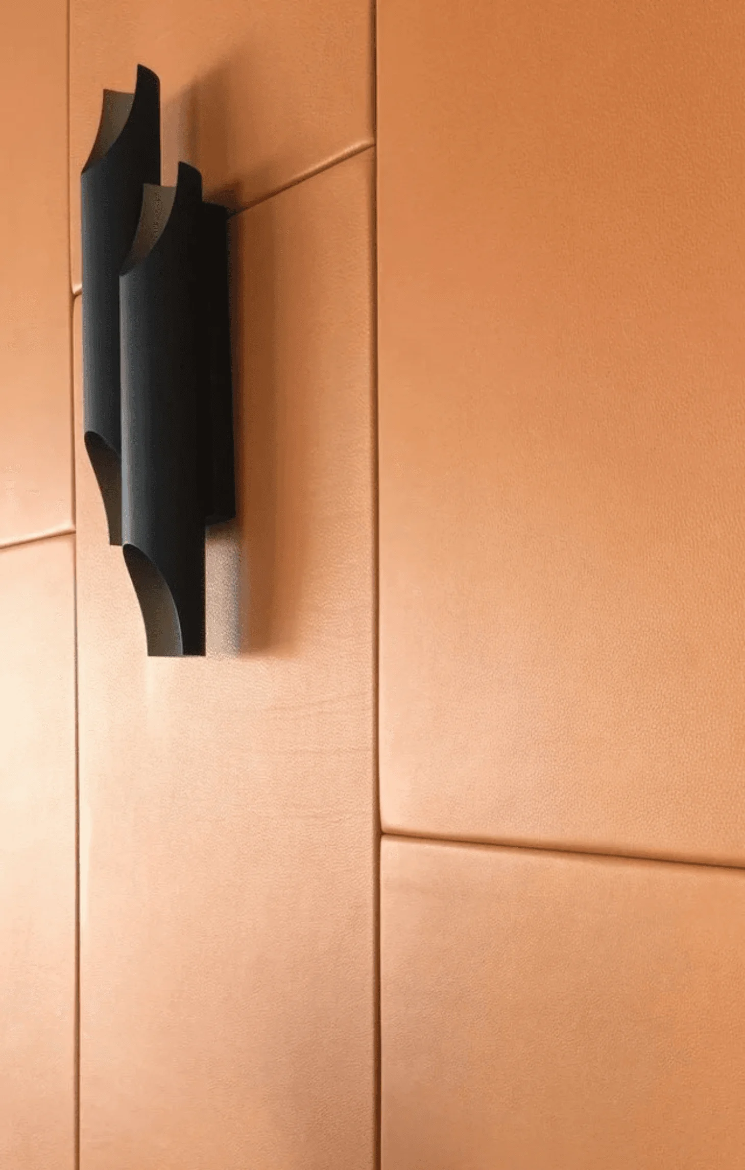 A close-up detail of the rust leather wall paneling and its sculptural black wall sconce