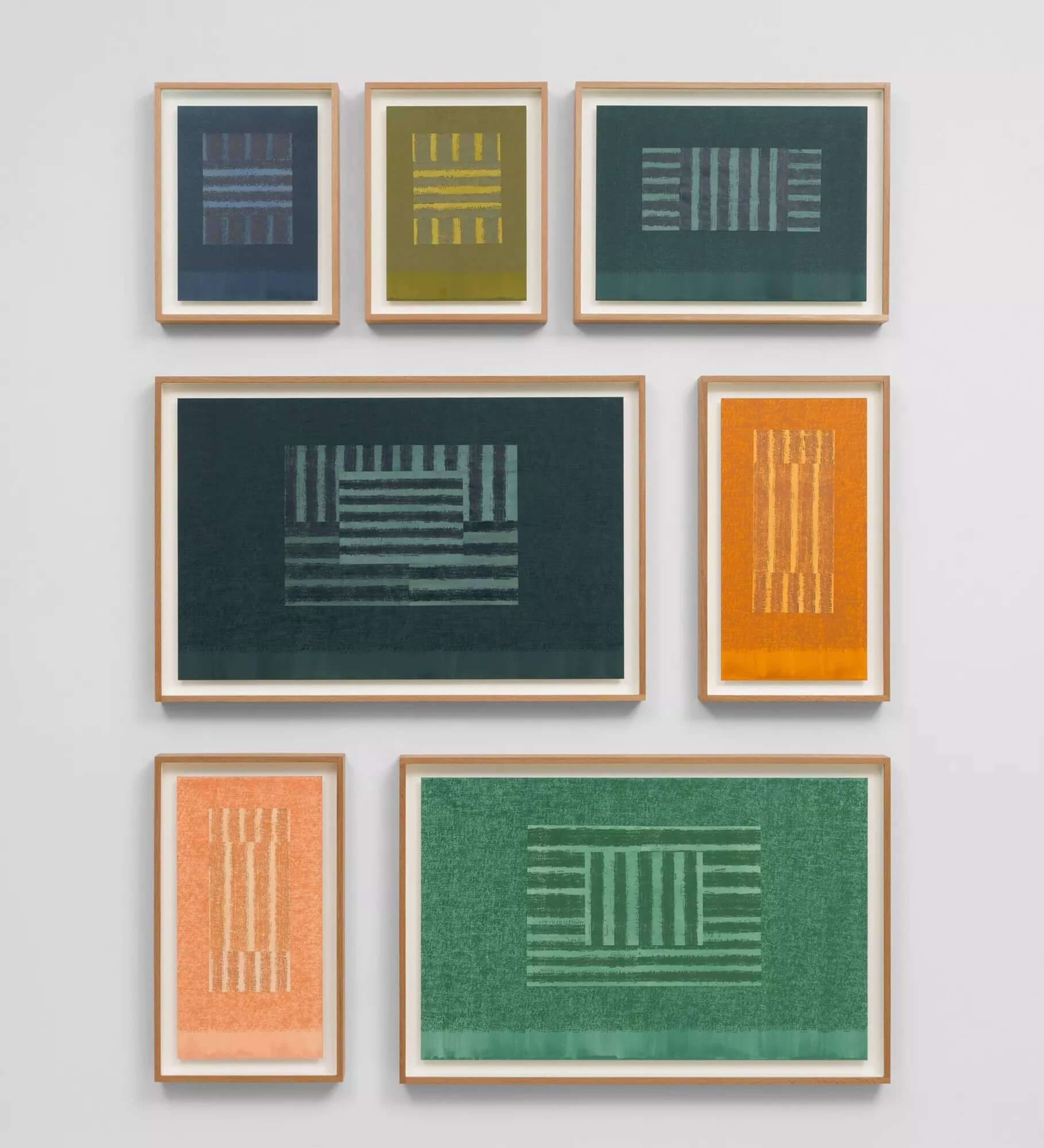 Wall display of framed geometric prints in green, blue, orange, and yellow tones arranged in a grid pattern.
