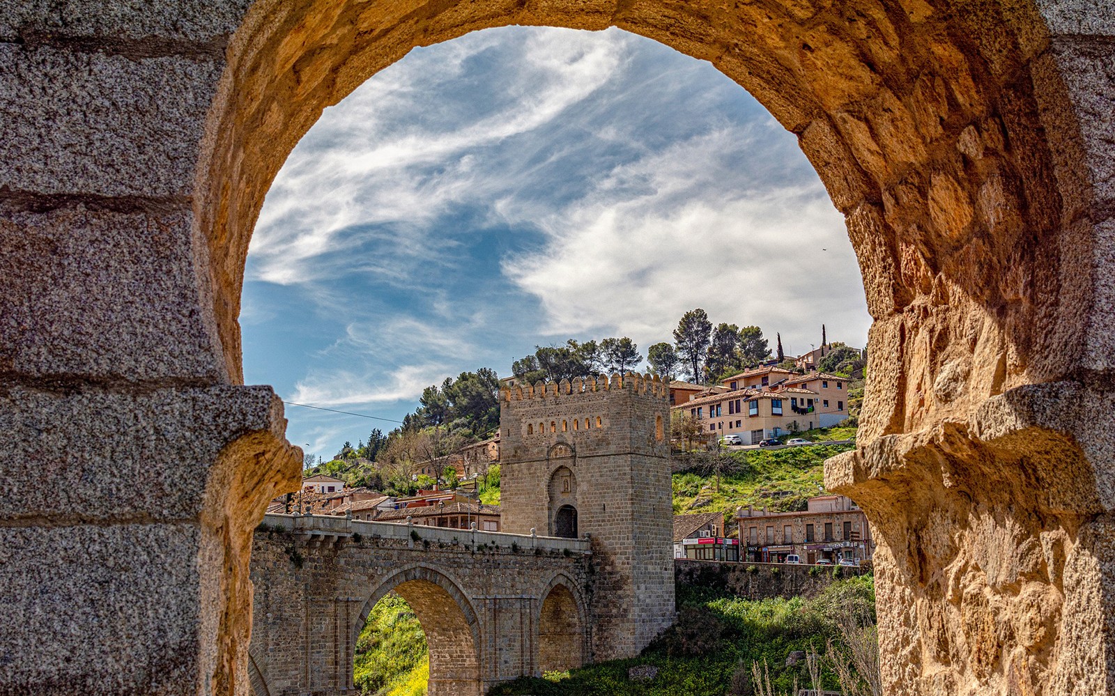 托萊多的阿爾坎塔拉門被石拱框住，背景是山坡上的房屋。