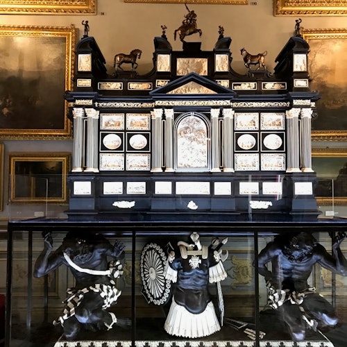 화려한 장식이 있는 전시물은 기둥과 동물 조각상이 위에 놓여 있고, 유리로 둘러싸인 아래쪽에는 인물들이 있는 정교한 구조입니다.