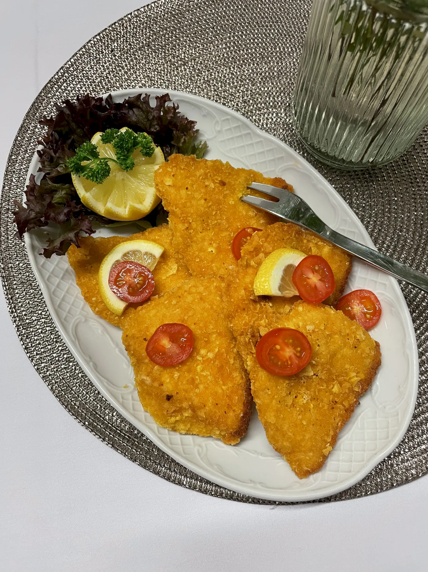 Hähnchenschnitzel garniert mit Tomaten, Zitronen und einem Blatt Salat.