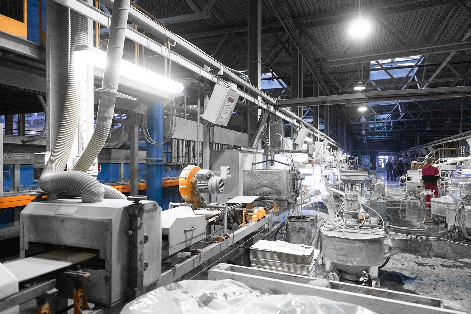 Industrielle Produktionshalle mit Maschinen, Förderbändern und Arbeitern an einer Fertigungslinie unter einer hohen Hallendecke