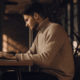 Man in turtleneck typing on laptop in warm office light