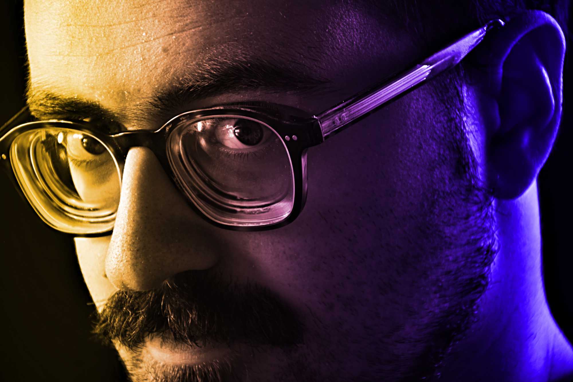 Le visage d'un jeune homme portant des lunettes, regardant un écran d'ordinateur.