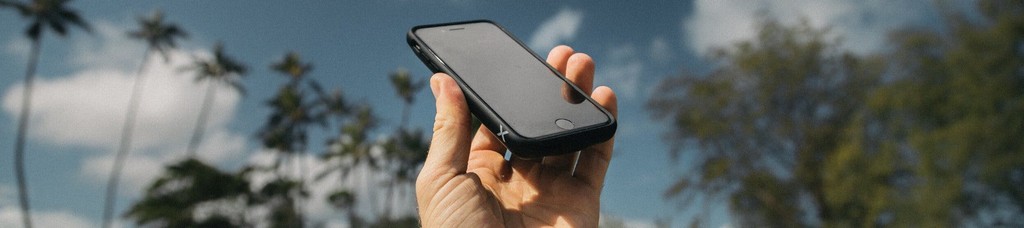Hand holding smartphone against blurred sky and trees background.