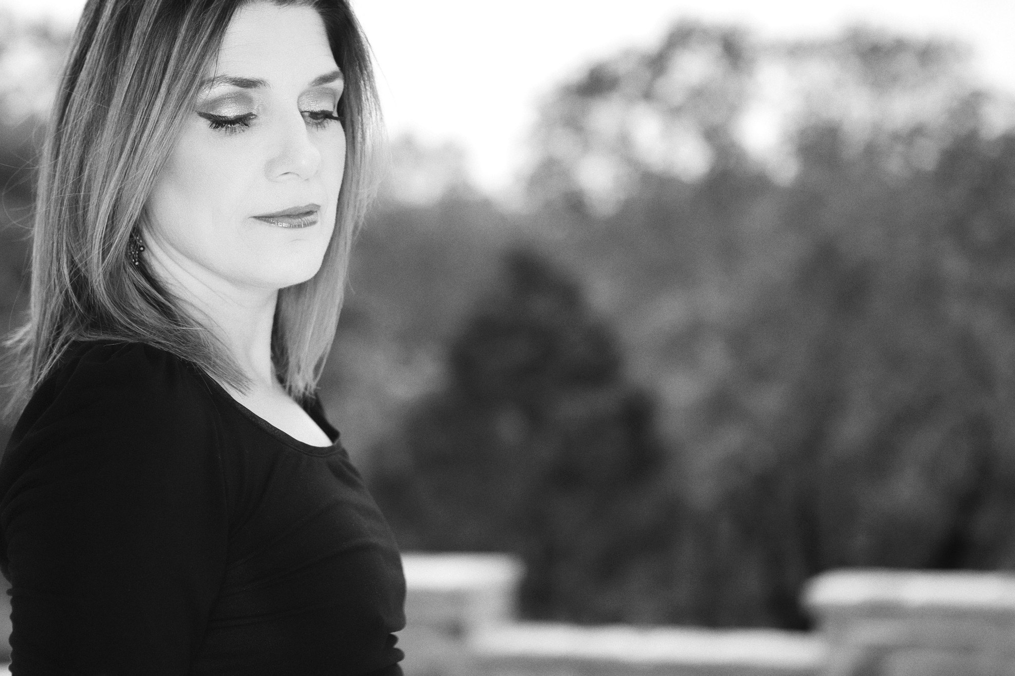 Black and white editorial portrait of a woman in profile, softly lit, with a blurred natural background.