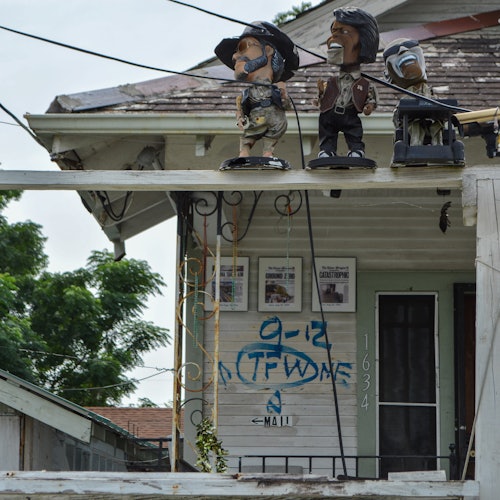 在门廊屋顶上有三个雕像的房子，墙上涂鸦写着"9-12 N.F.D.W.N.E."，地址显示为"1634"。