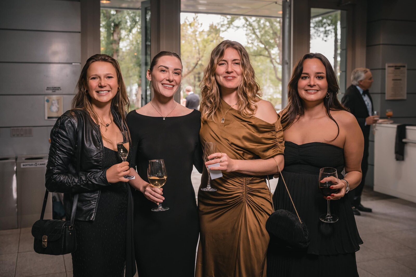Four guests in evening dresses holding wine glasses at an indoor reception