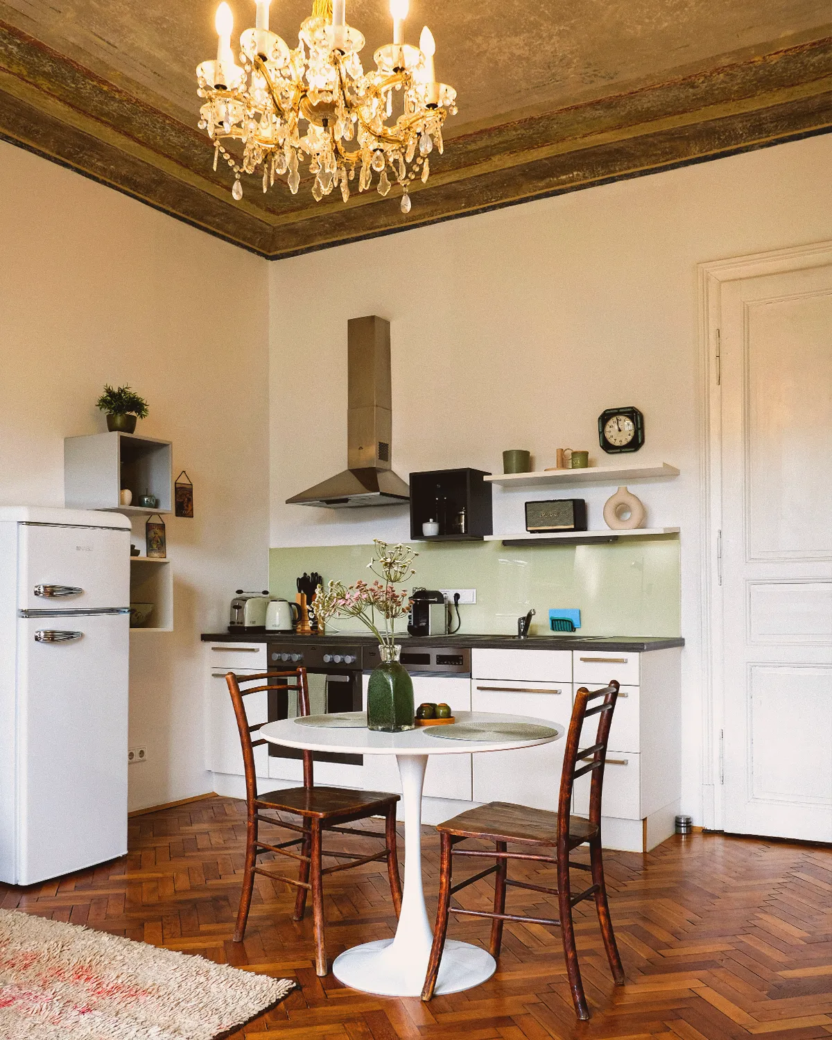 Boutique N°2 • kitchen with a white tulip table, wooden chairs, a cream retro fridge and a crystal chandelier