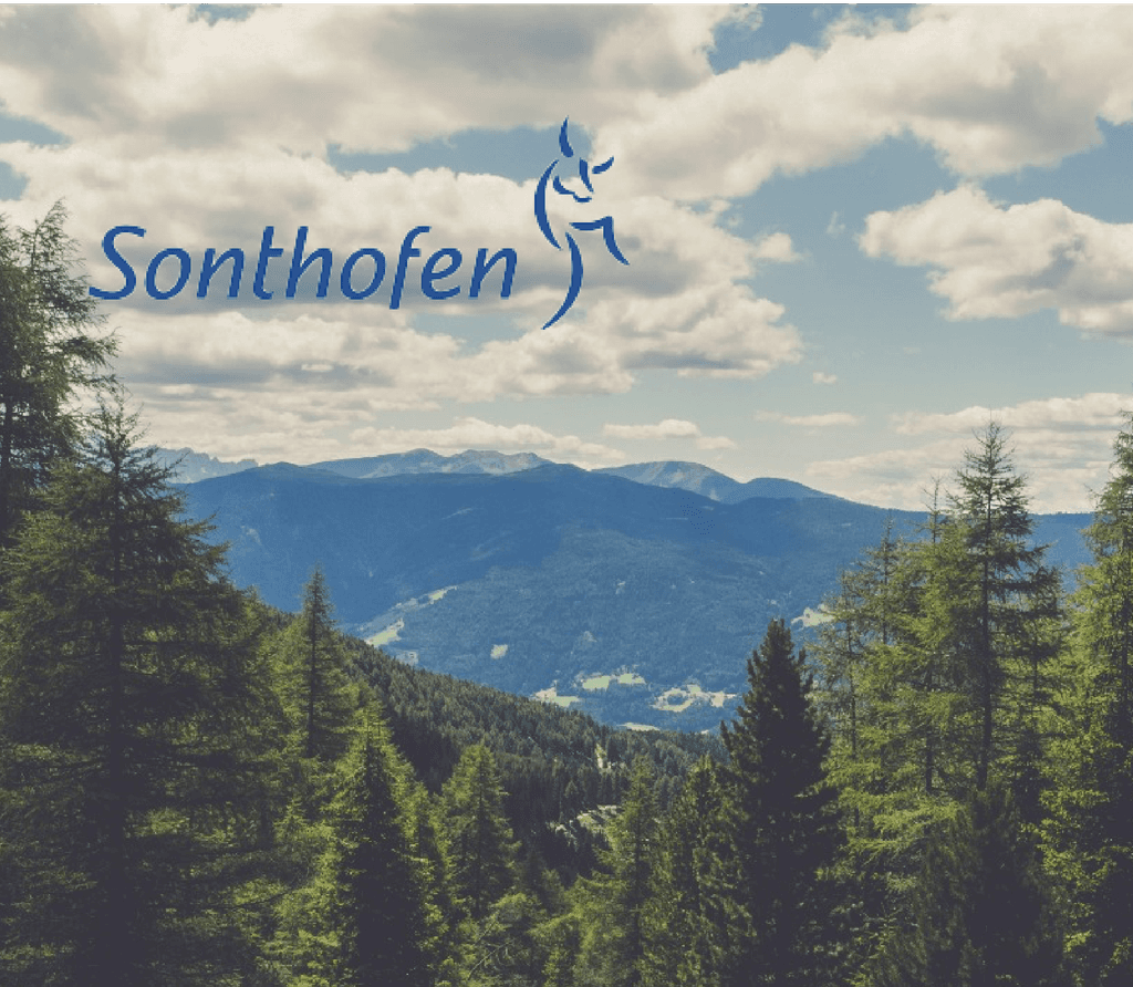 In der Ferne ist eine große Berglandschaft zu sehen, im Vordergrund ein Waldabschnitt mit riesigen Tannen und darauf befindet sich das Logo der Stadt Sonthofen