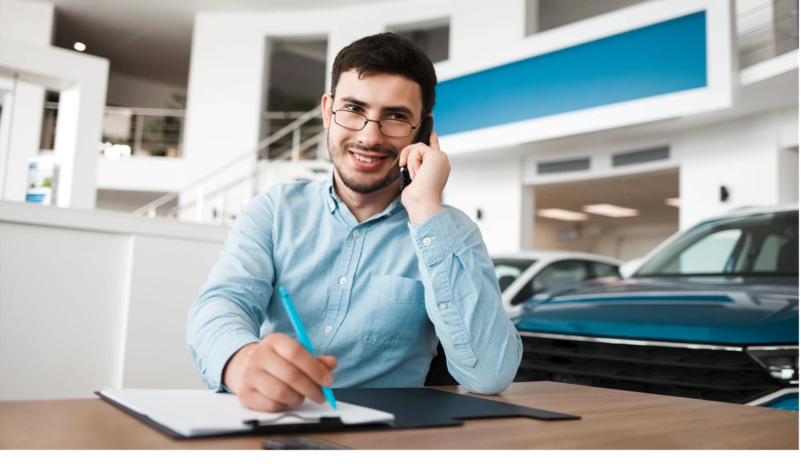 Auto dealership employee talking on the phone and writing