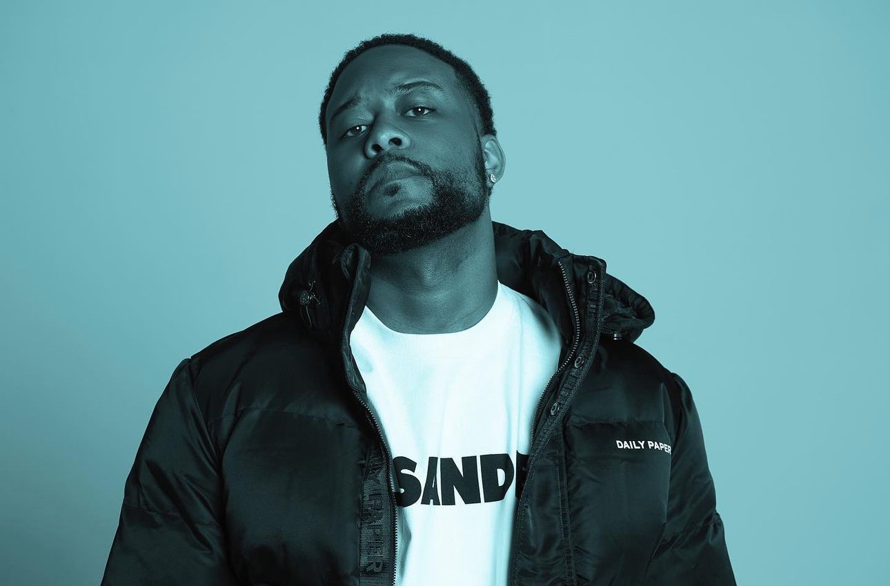 Supah Mario, music producer for Young Thug, Lil Uzi Vert, and Drake, poses in a blue-tinted portrait wearing a black jacket and white t-shirt.