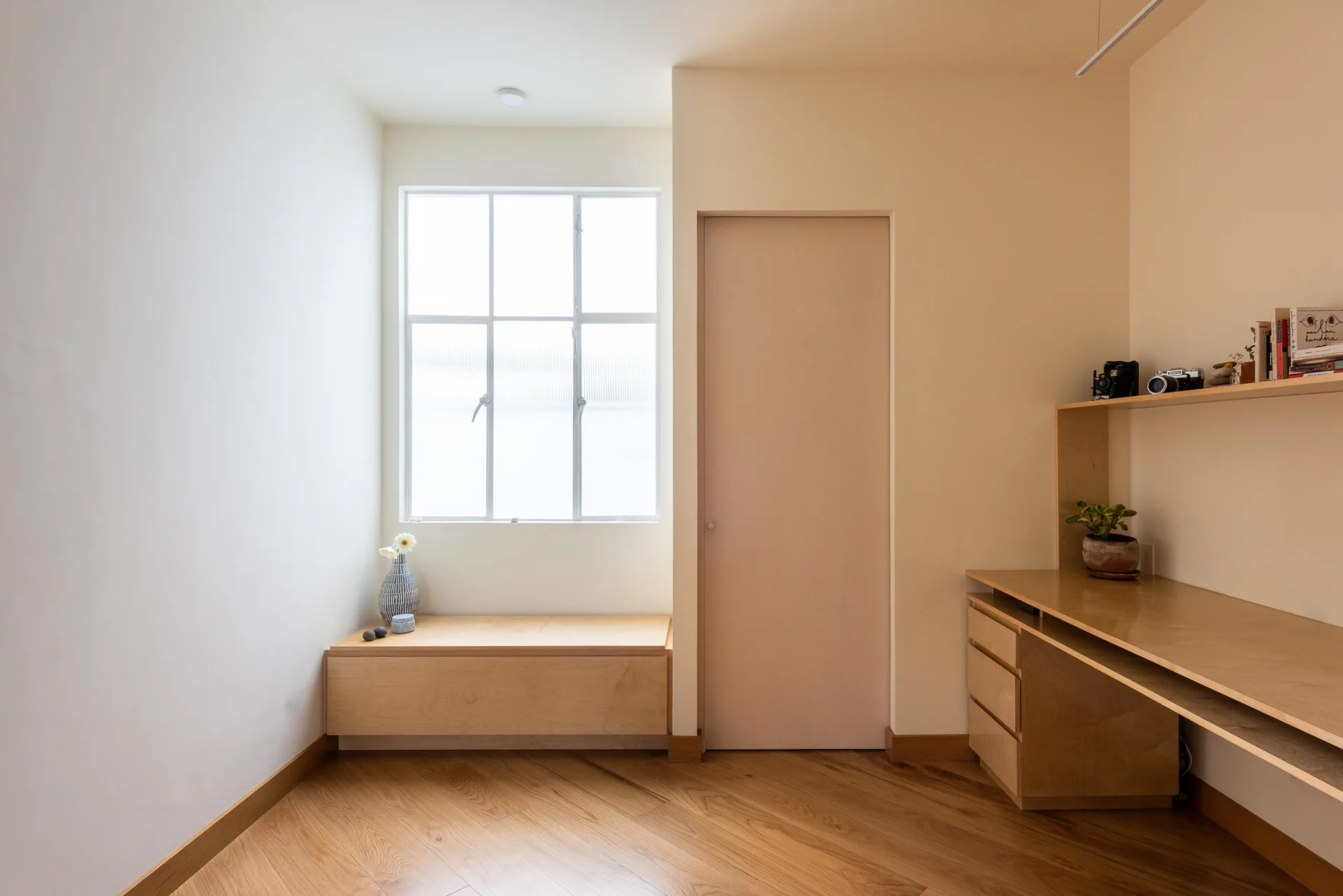 Estudio con escritorio empotrado de madera y banca bajo la ventana