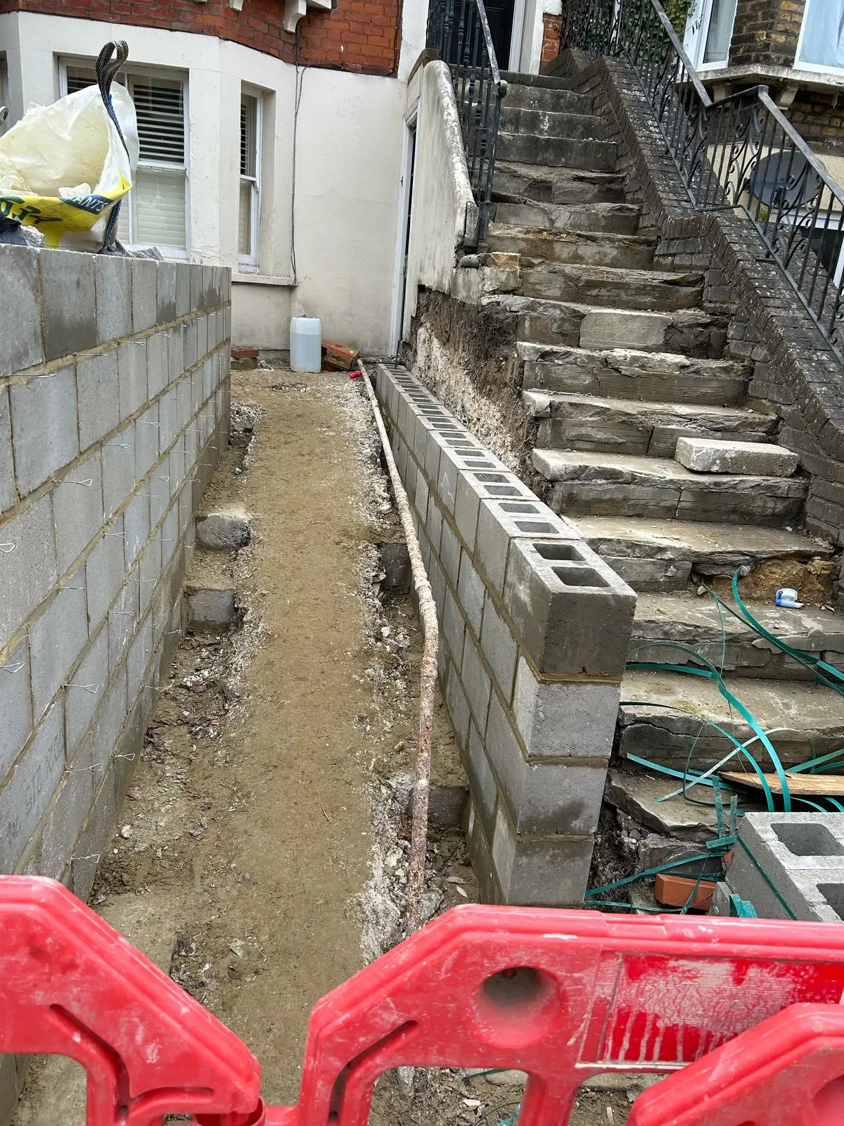 Construction site with unfinished stairs and a pathway, marked with red safety barriers.