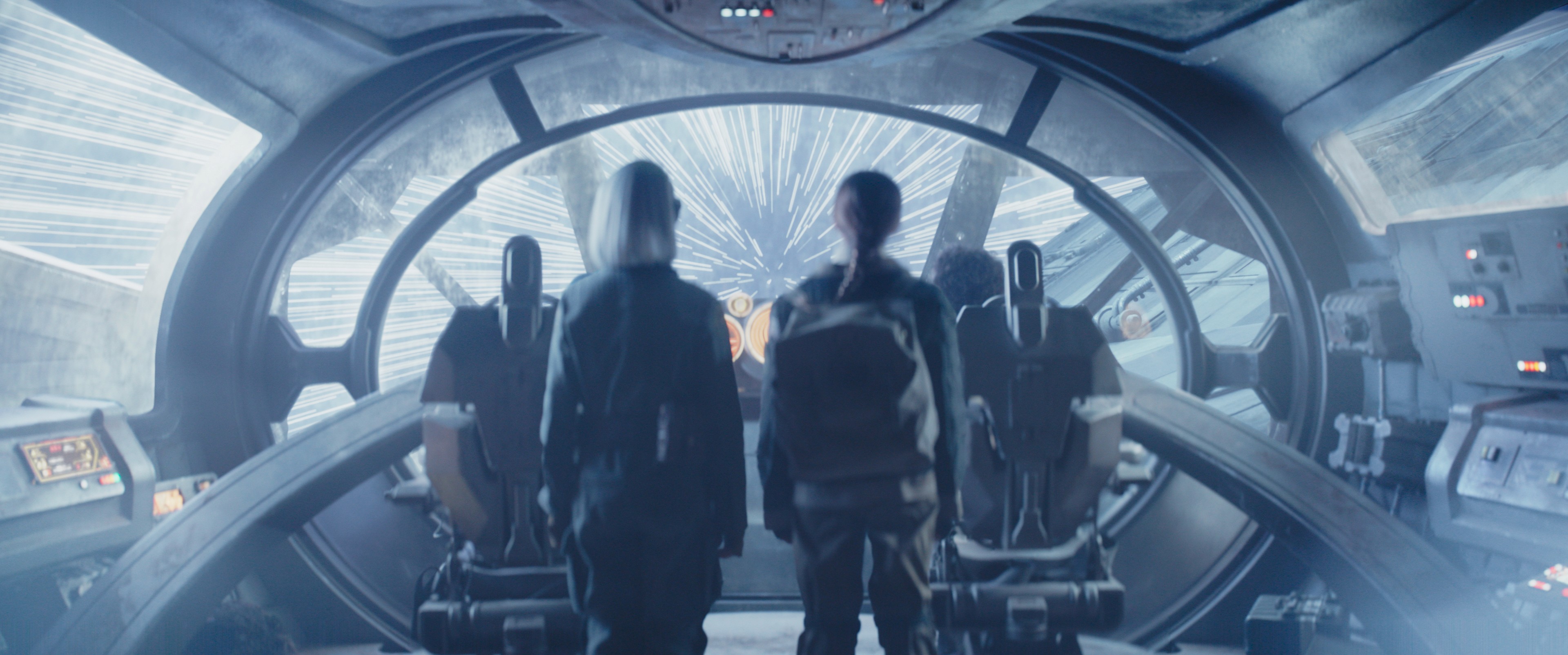 Two young people stand in a futuristic cockpit, looking out at a hyperspace transit.