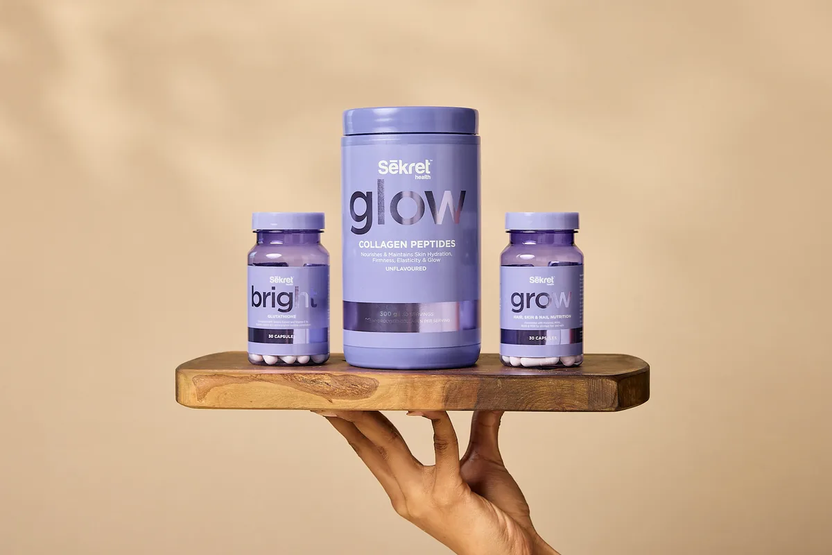 The Sēkret Glow collagen tub between Bright and Grow capsules on a wooden board