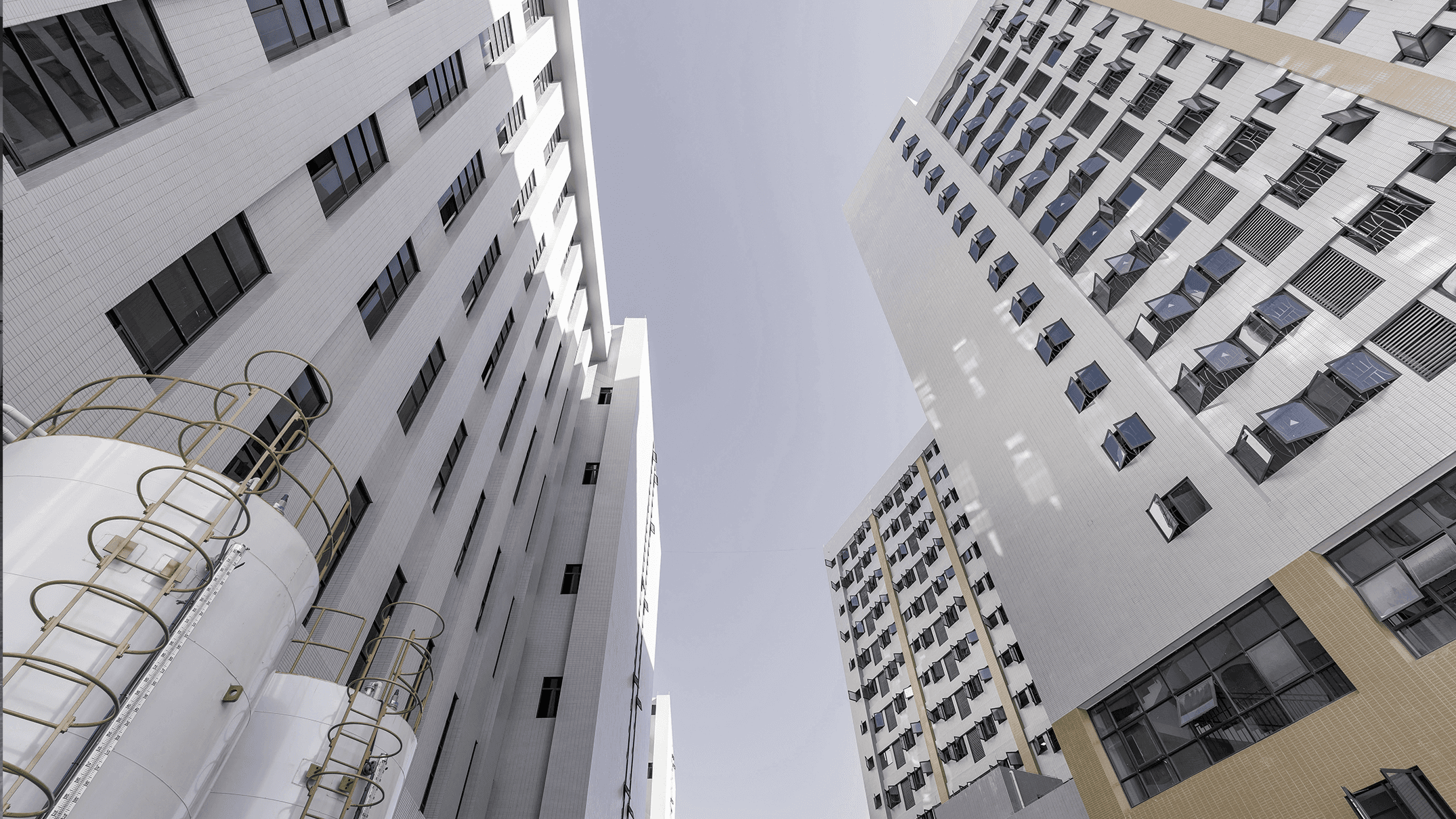 Exterior view of a large-scale modern office furniture factory complex featuring multi-story industrial buildings and storage silos under a clear sky.