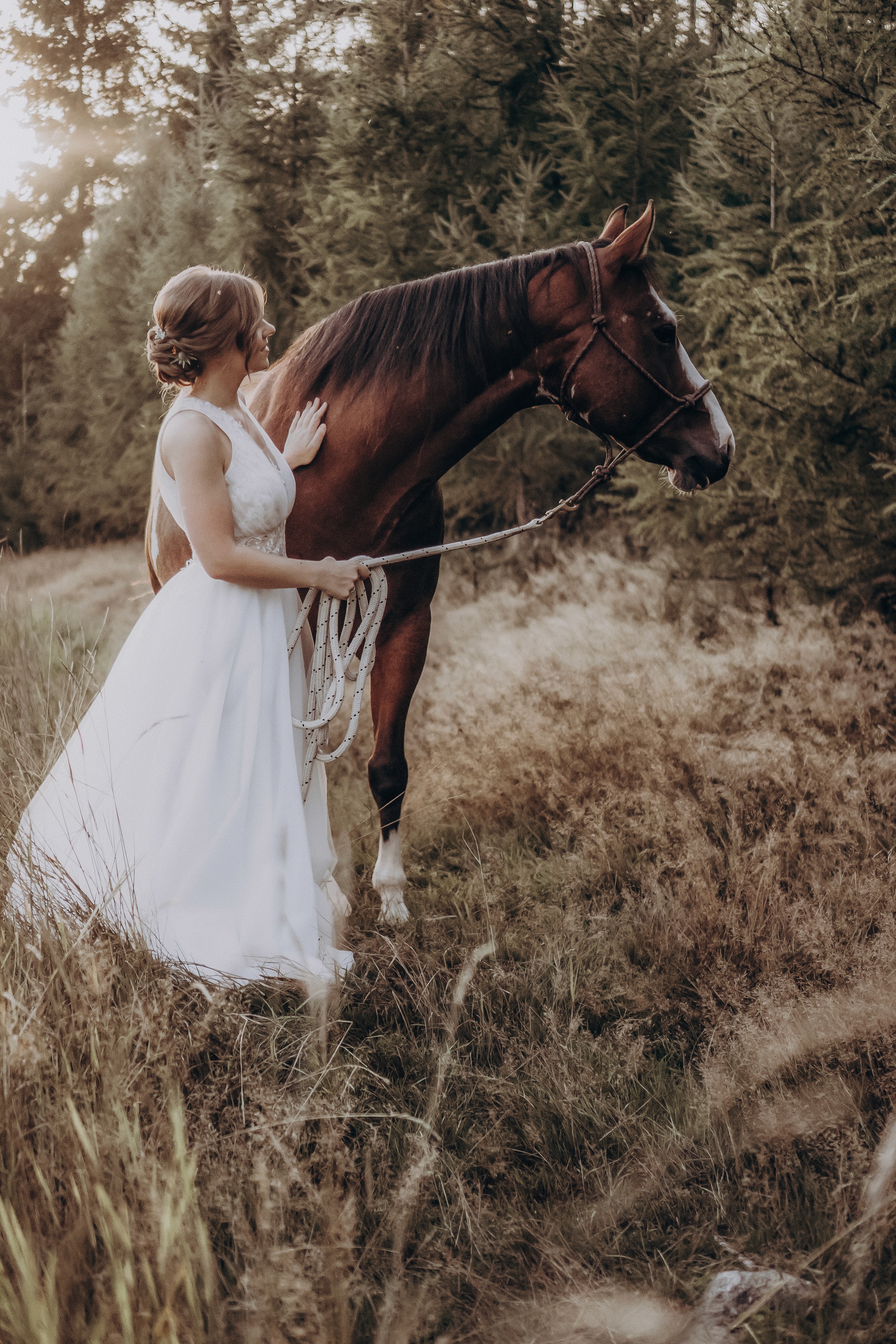 Braut im weißen Kleid steht mit einem braunen Pferd im Wald bei Bogen – Hochzeitsfotografie Bayern.