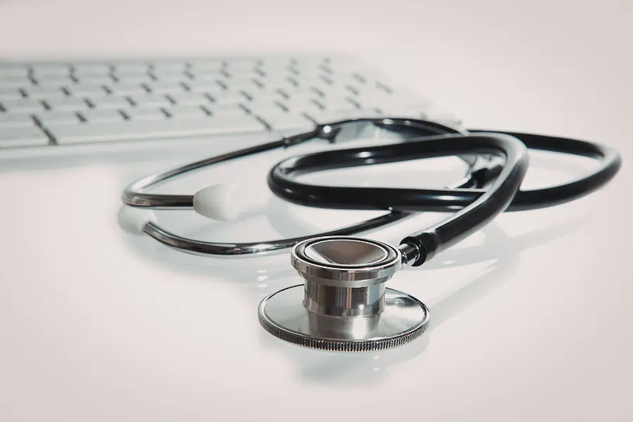 ai in medicine represented by a professional stethoscope laying on a white desk next to a computer keyboard.