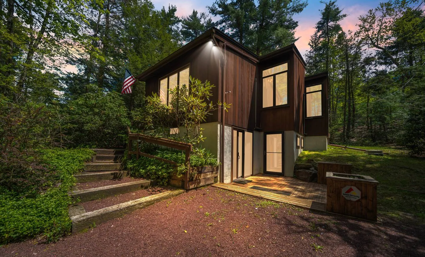 Modern wood-sided home with stone steps lit at dusk at Lake Front, Lake Naomi, Pocono Pines, PA