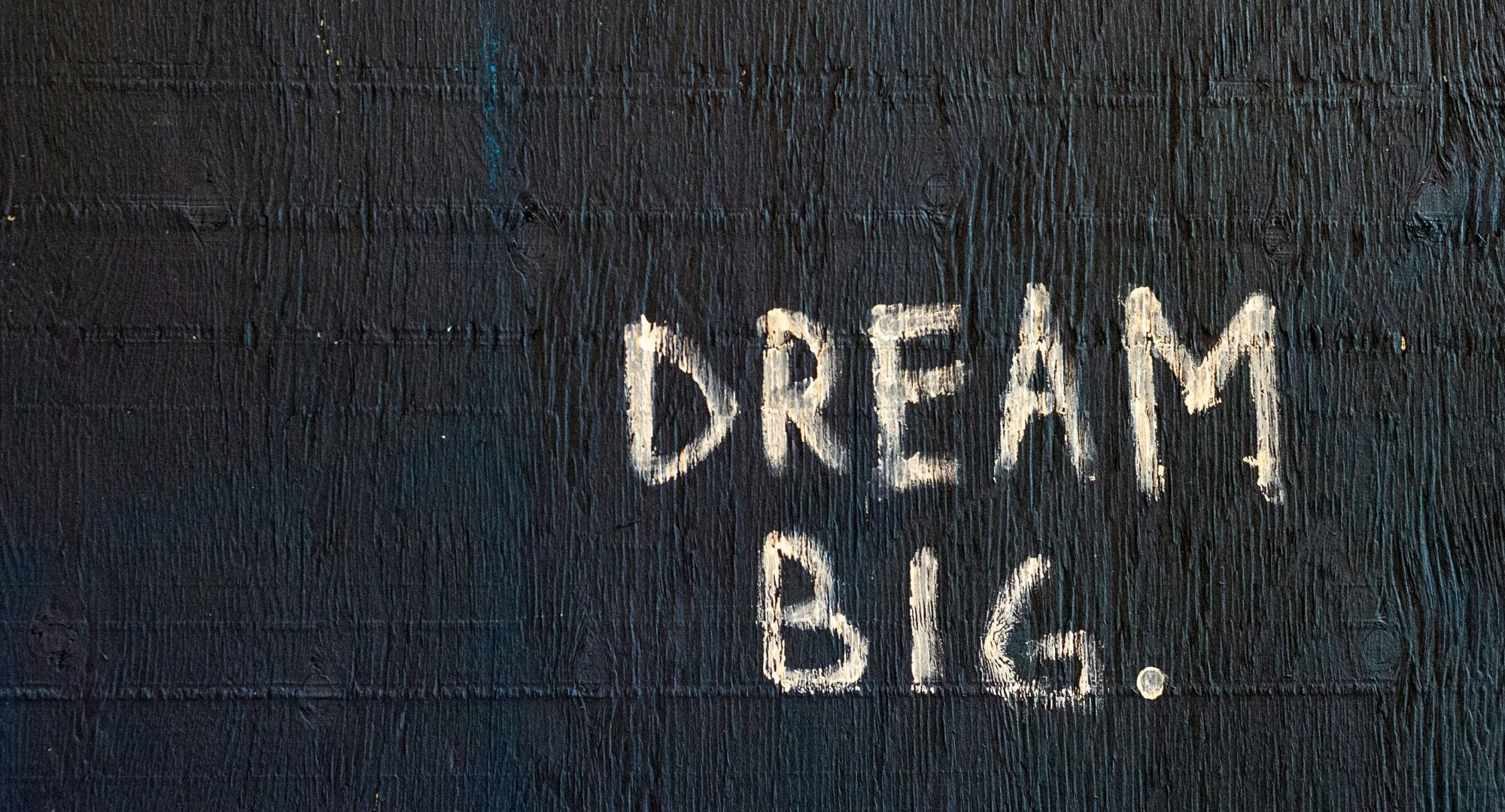 parede preta com "DREAM BIG." rabiscado com tinta nela