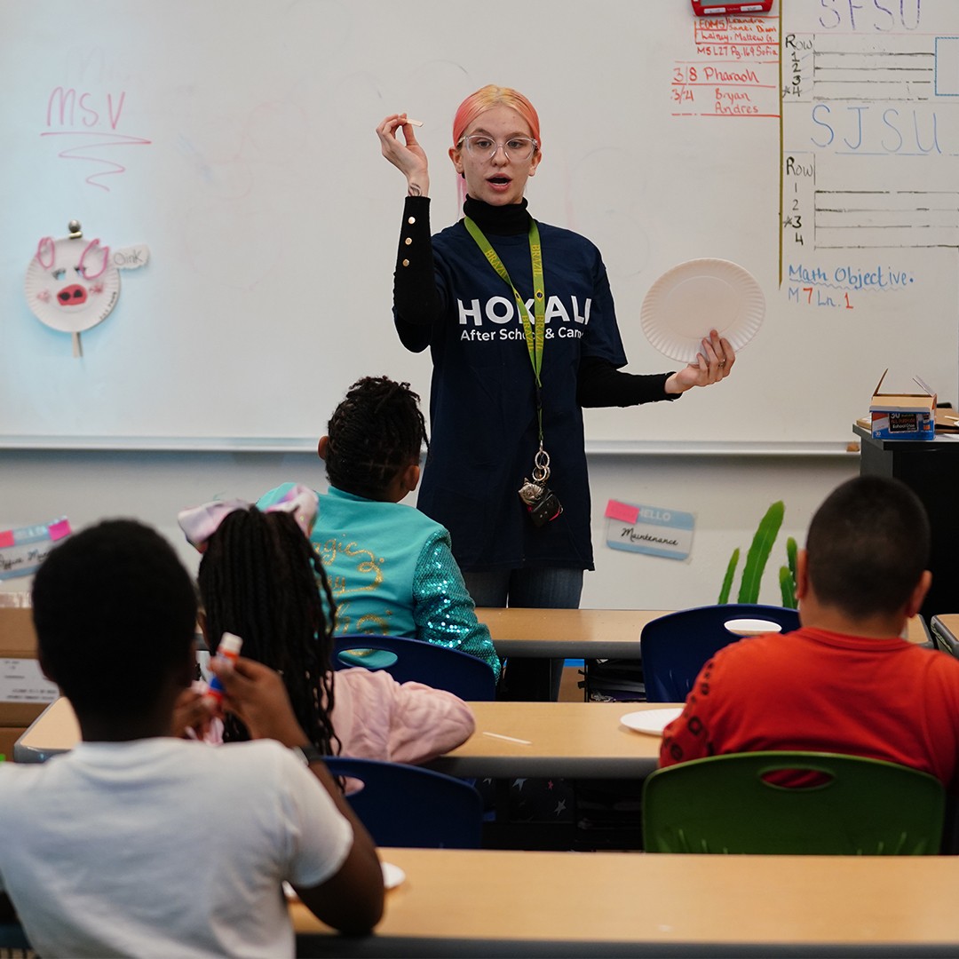 Art educator teaching painting techniques to students in enrichment workshop