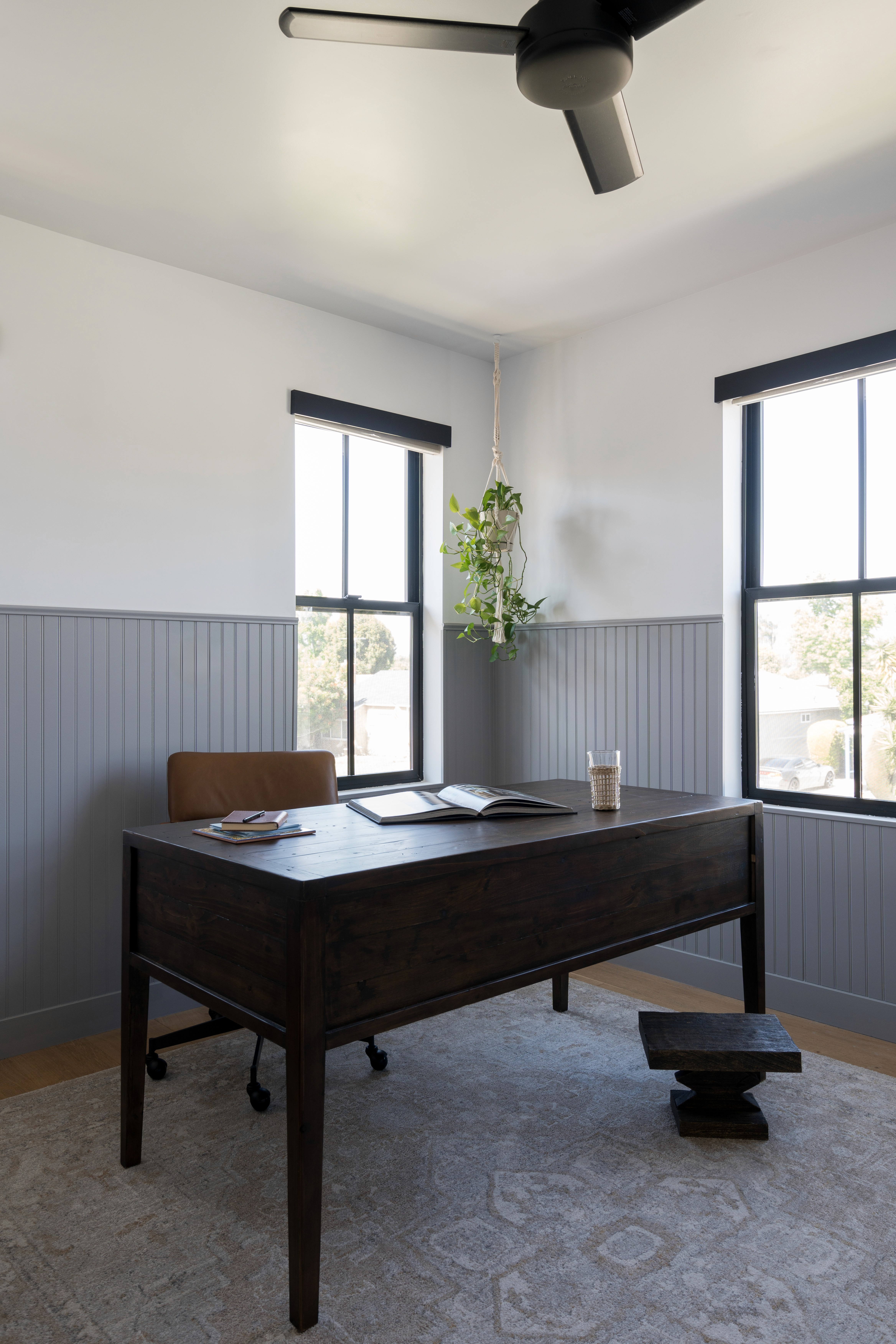 A stylish and functional workspace featuring a modern desk with ample surface area. The room is adorned with neutral tones, accented by wooden elements and lush greenery, creating a serene environment conducive to productivity by Jubilee Interiors in Lakewood, California