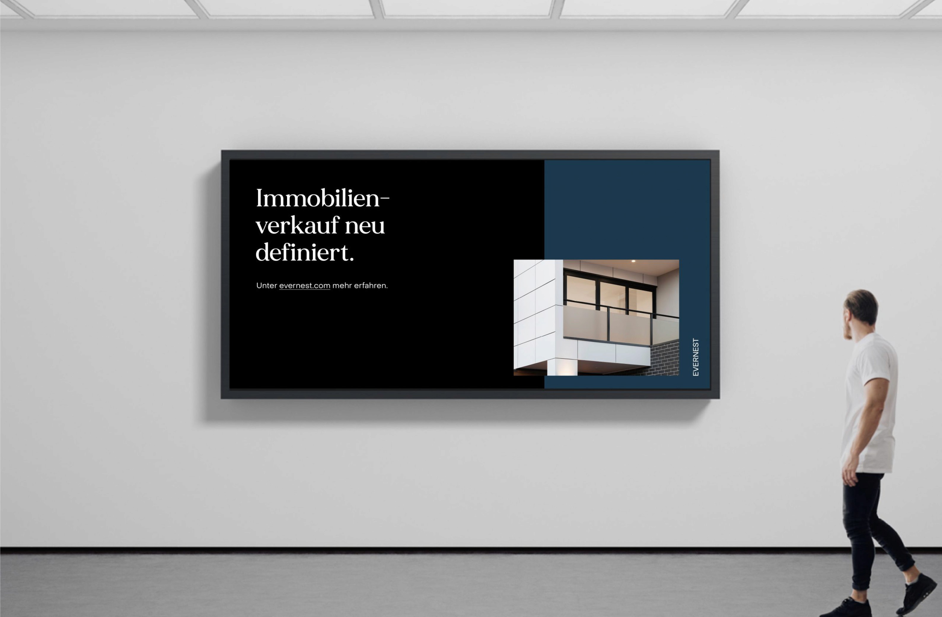 A person standing next to a large digital display advertising "Immobilienverkauf neu definiert" with an architectural image, promoting Evernest.com.