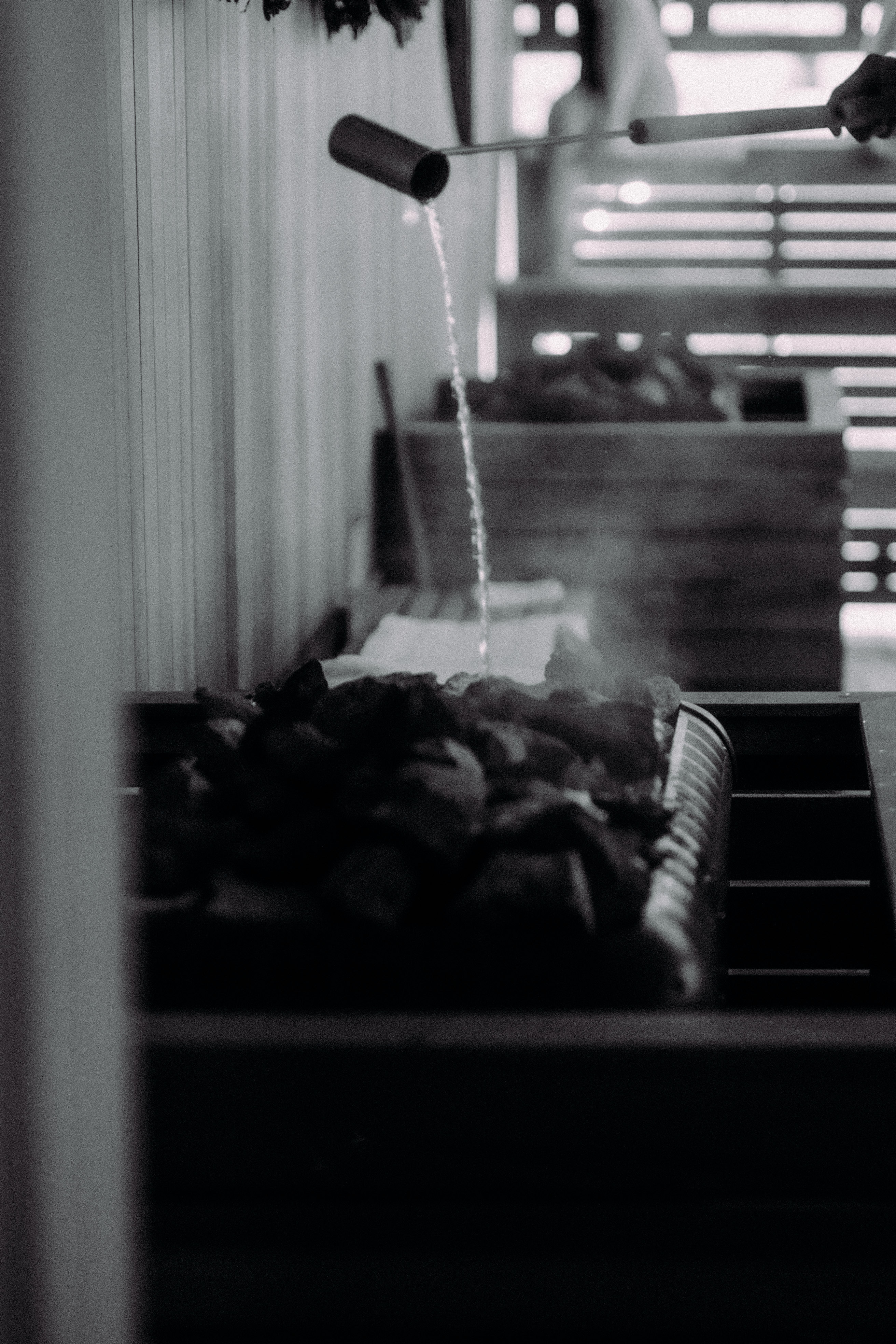 Black and white image of a sauna interior with stacked wooden benches and a stove holding a bucket for essential oil aromatherapy