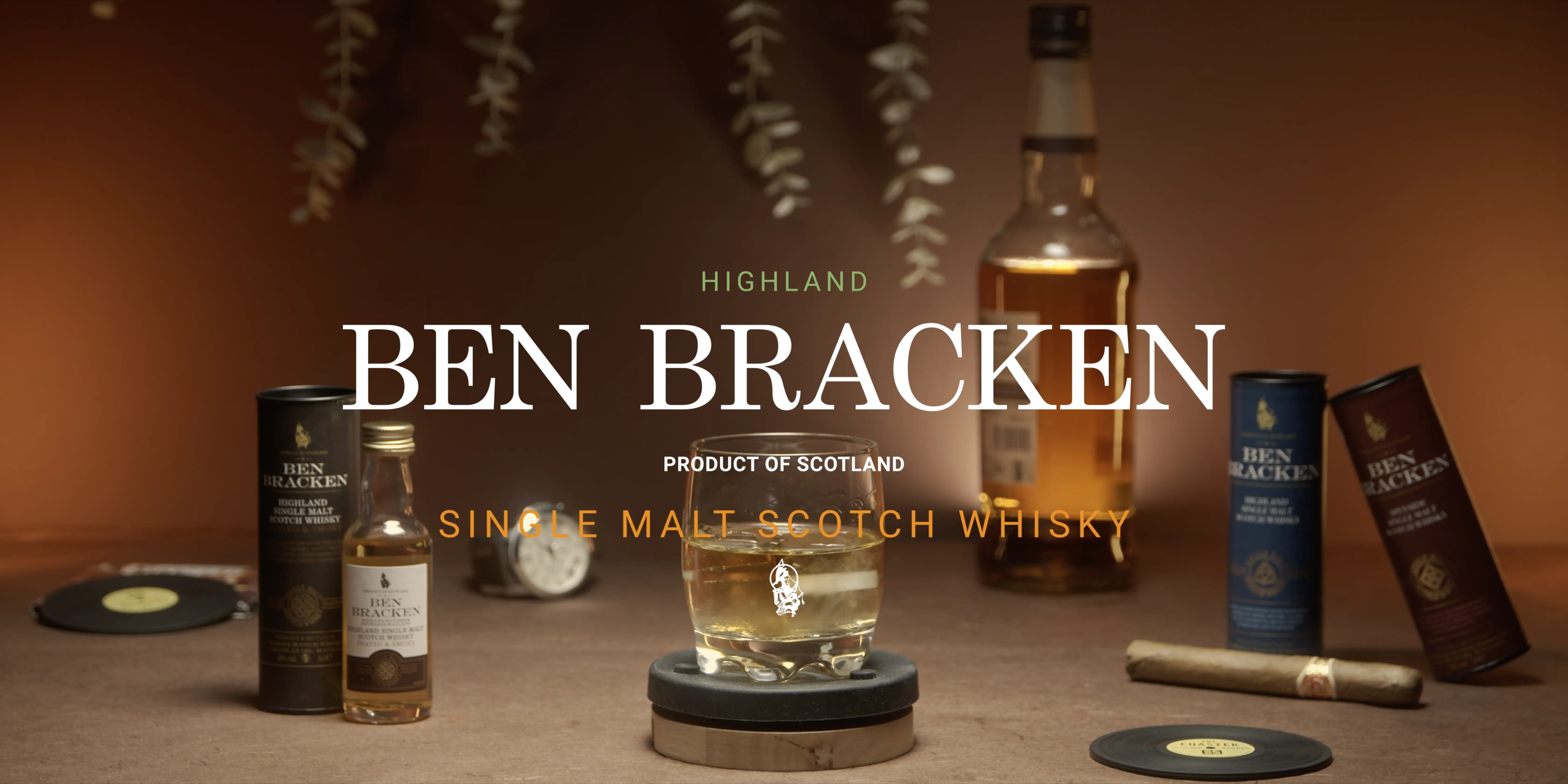 A bottle and glass of Ben Bracken Highland Single Malt Scotch Whisky are prominently displayed on a textured wooden surface, with two cylindrical boxes, a coaster, and a cigar adding an elegant touch against a warm, softly lit background.