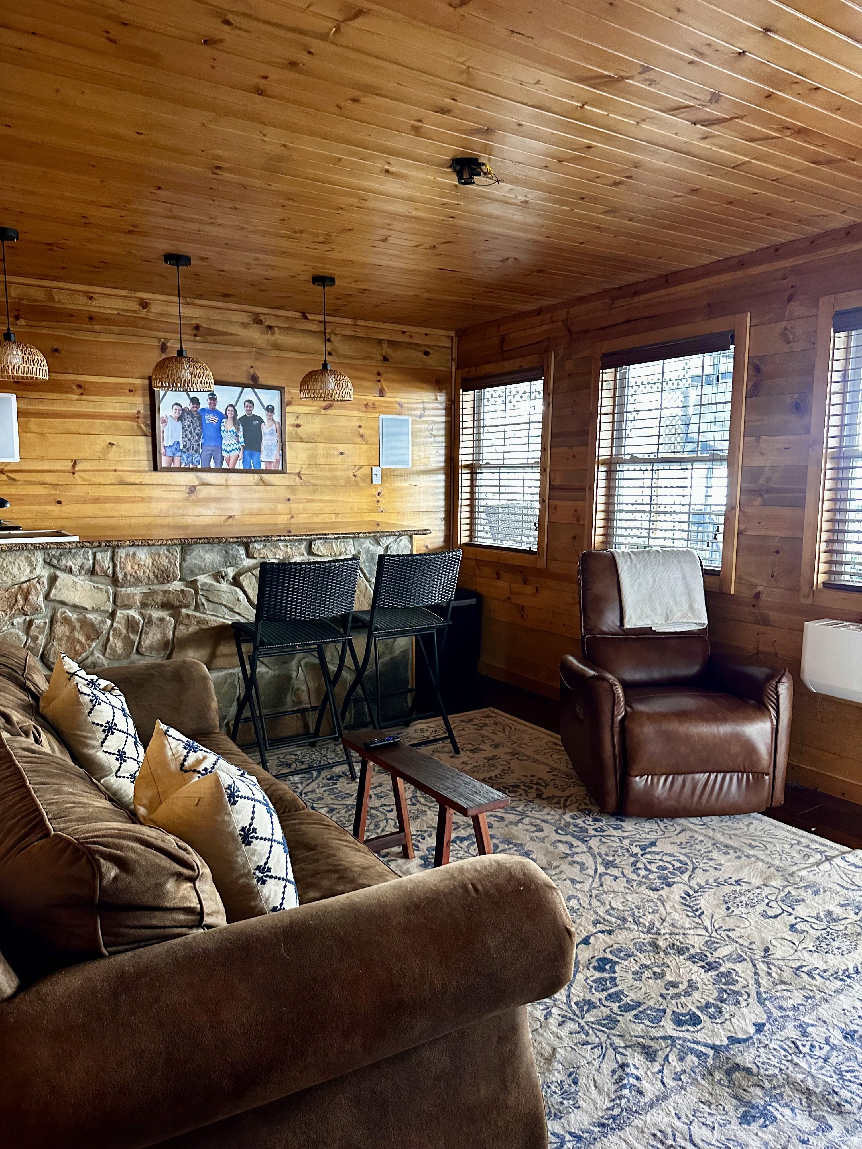 Cozy cabin living room with wooden walls, bar, brown sofa, leather recliner, and decorative rug. A perfect space for relaxation.