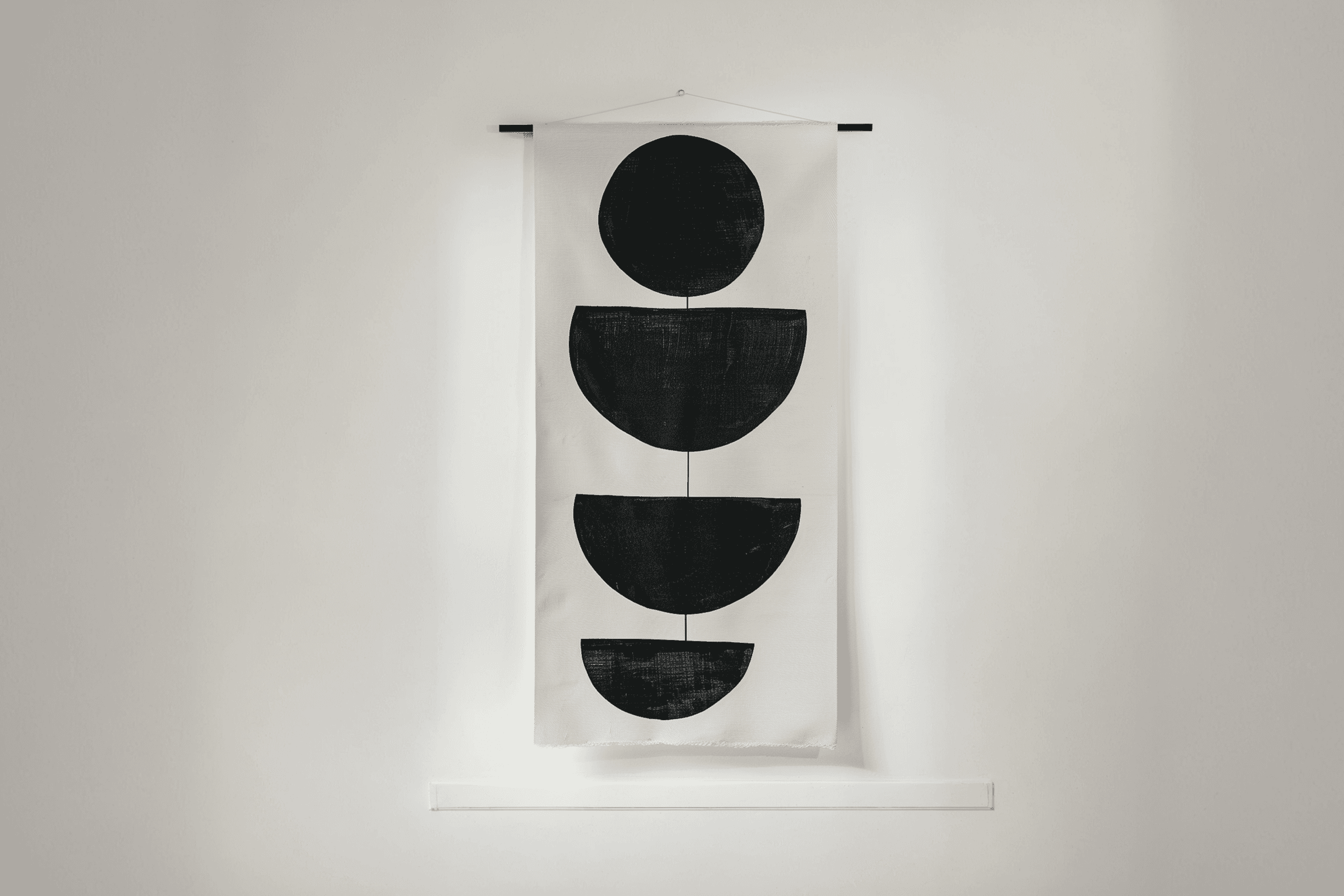 Minimalist wall hanging with black geometric shapes on white canvas, featuring a circle and half-circles connected by lines.