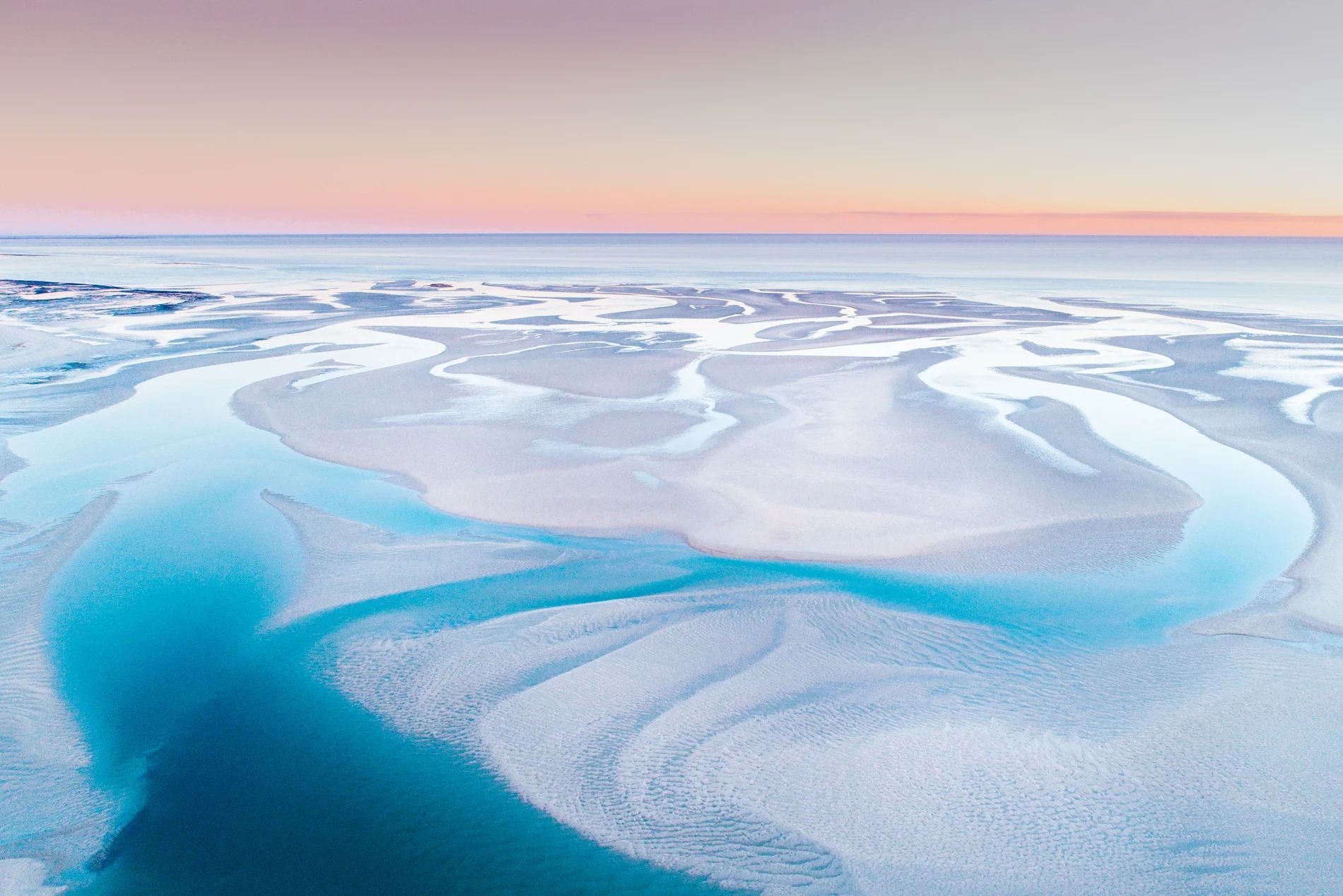 Aerial of tidal channels winding between pale sandbanks at dawn
