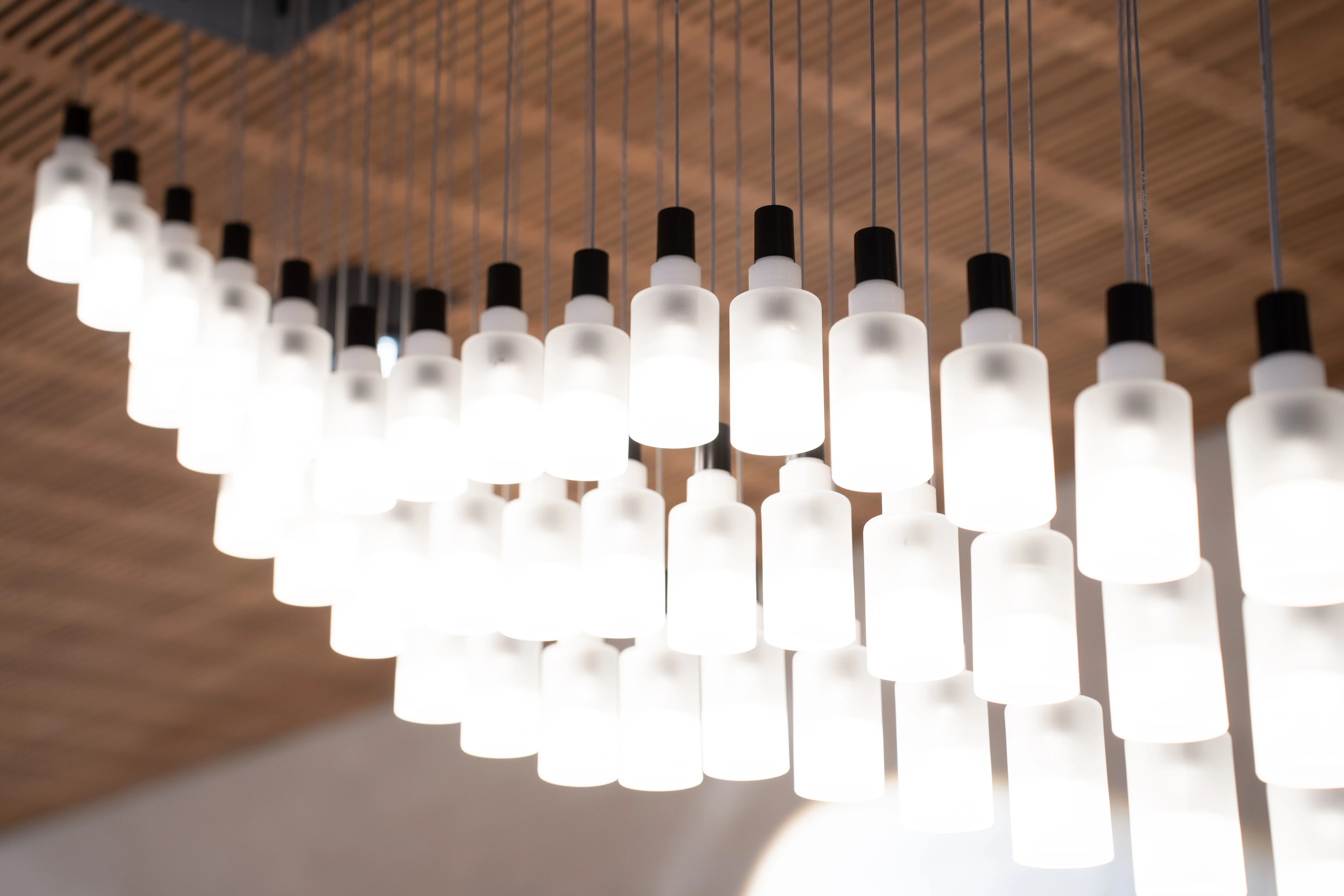 Detail of the pendant light installation at EMPL FRISEURE with rows of frosted glass cylinders hanging from a wooden grid ceiling.