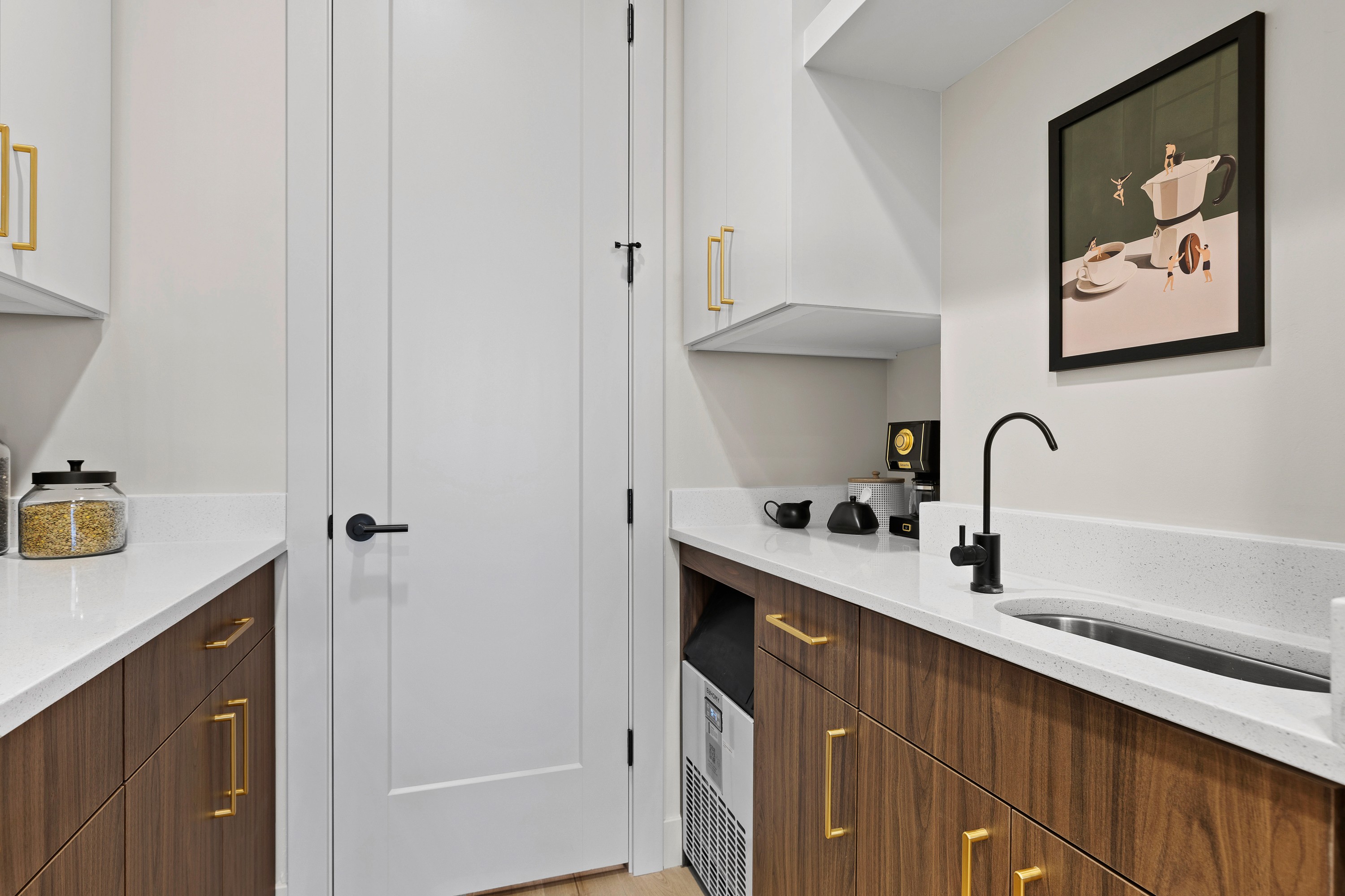 Butler pantry in a Southern Utah custom home with two-toned cabinets, quartz countertops, an ice maker, and a drink sink, showcasing functional storage and design details.