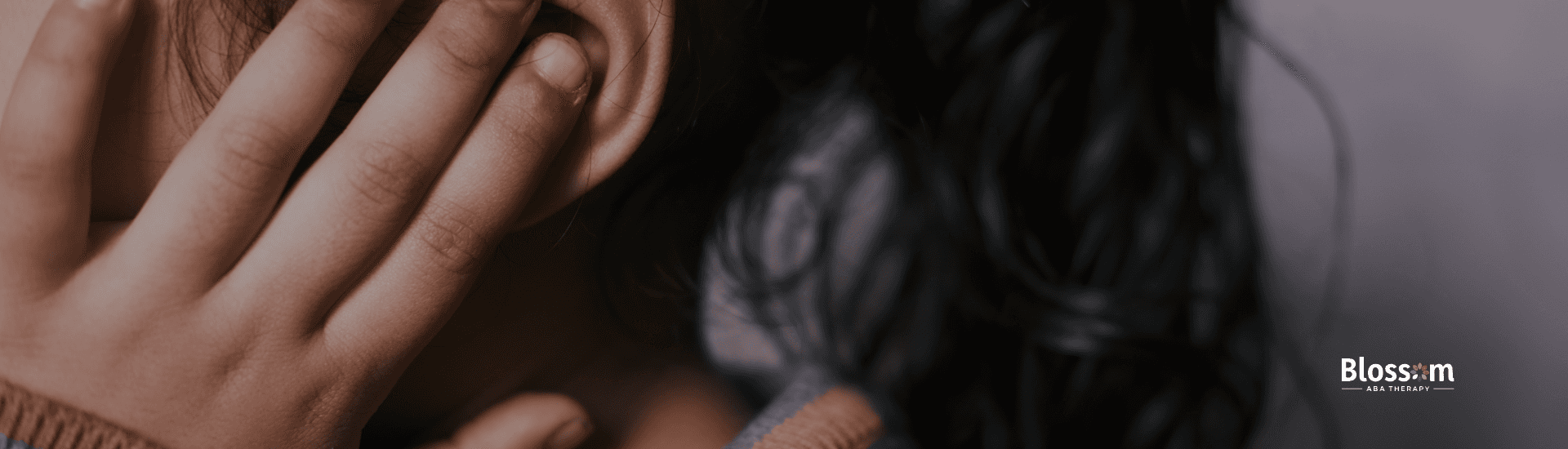 Child covering their ears, illustrating sensory sensitivity to sound, with the Blossom ABA Therapy logo visible in the background.