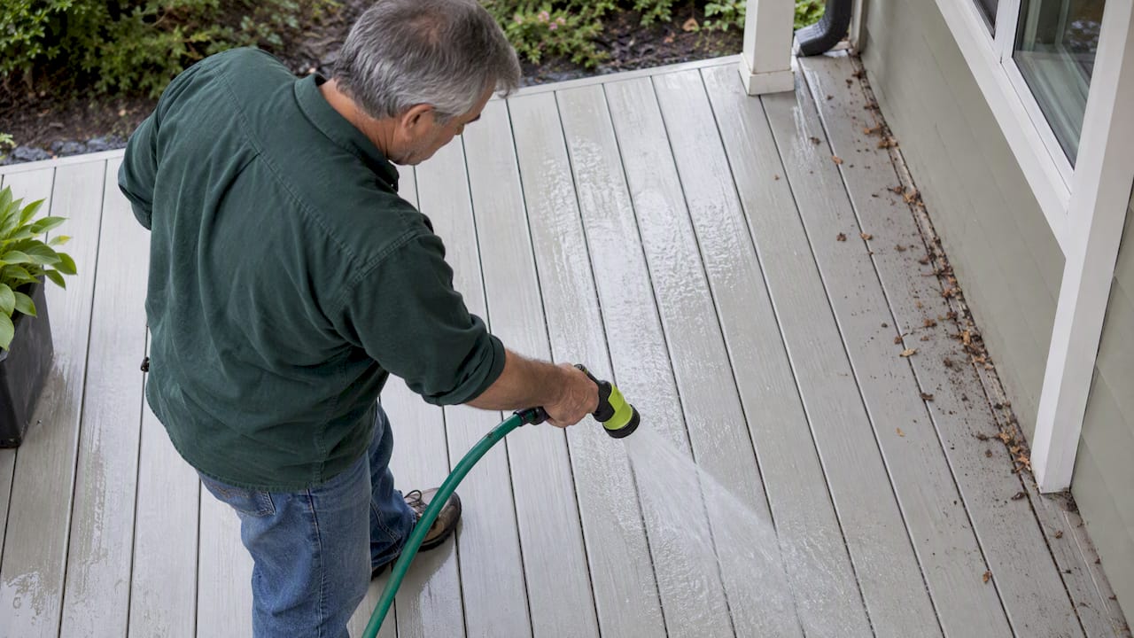 Homeowner rinsing pollen from pale deck boards