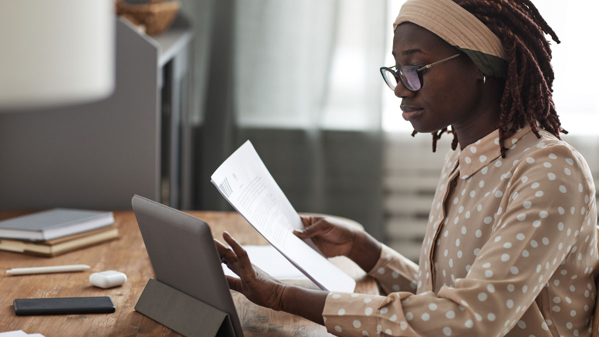 A woman sitting at her desk, reading and taking notes on her iPad