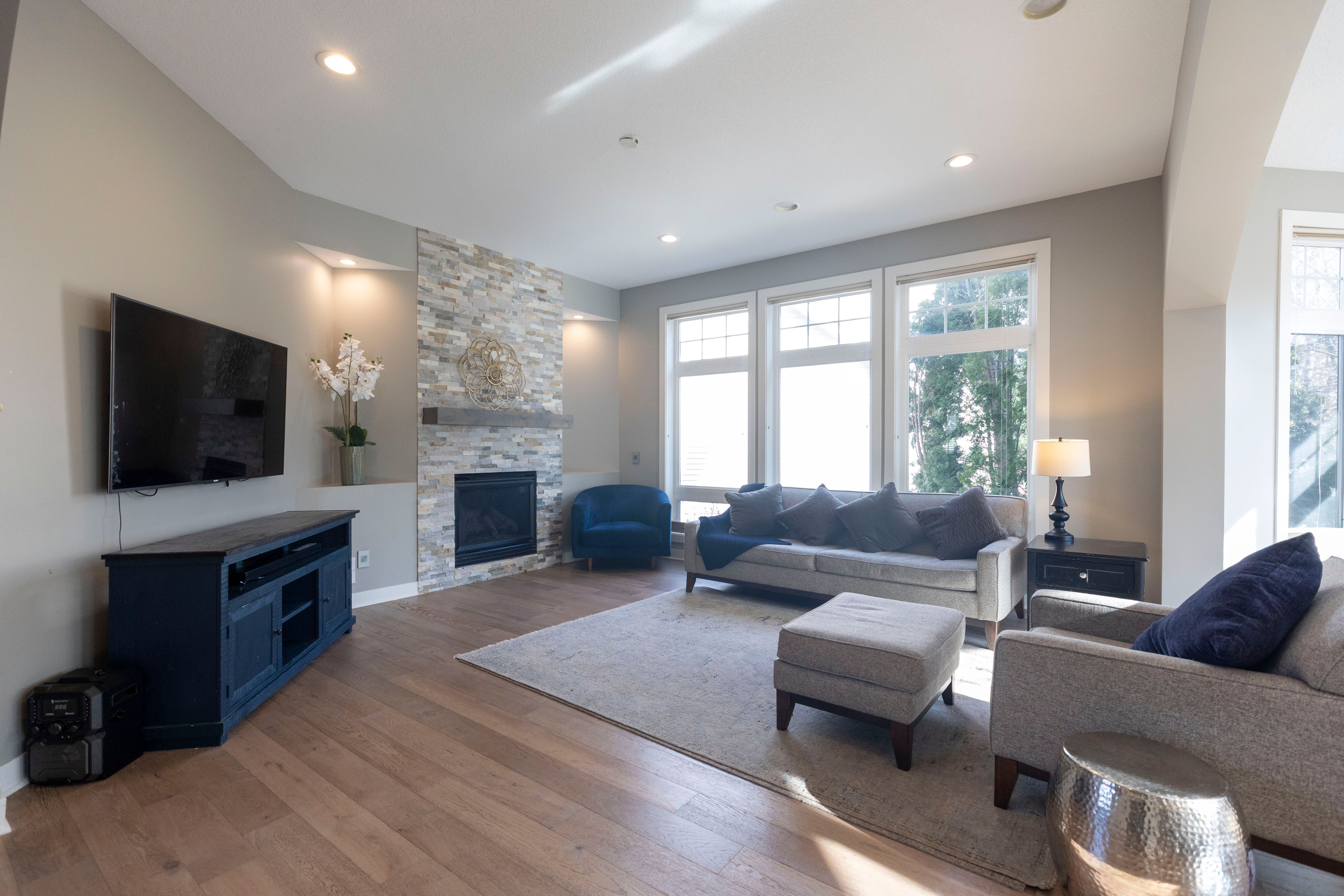 Bright, open-concept living room with a mounted TV, gray sofa, and large windows.